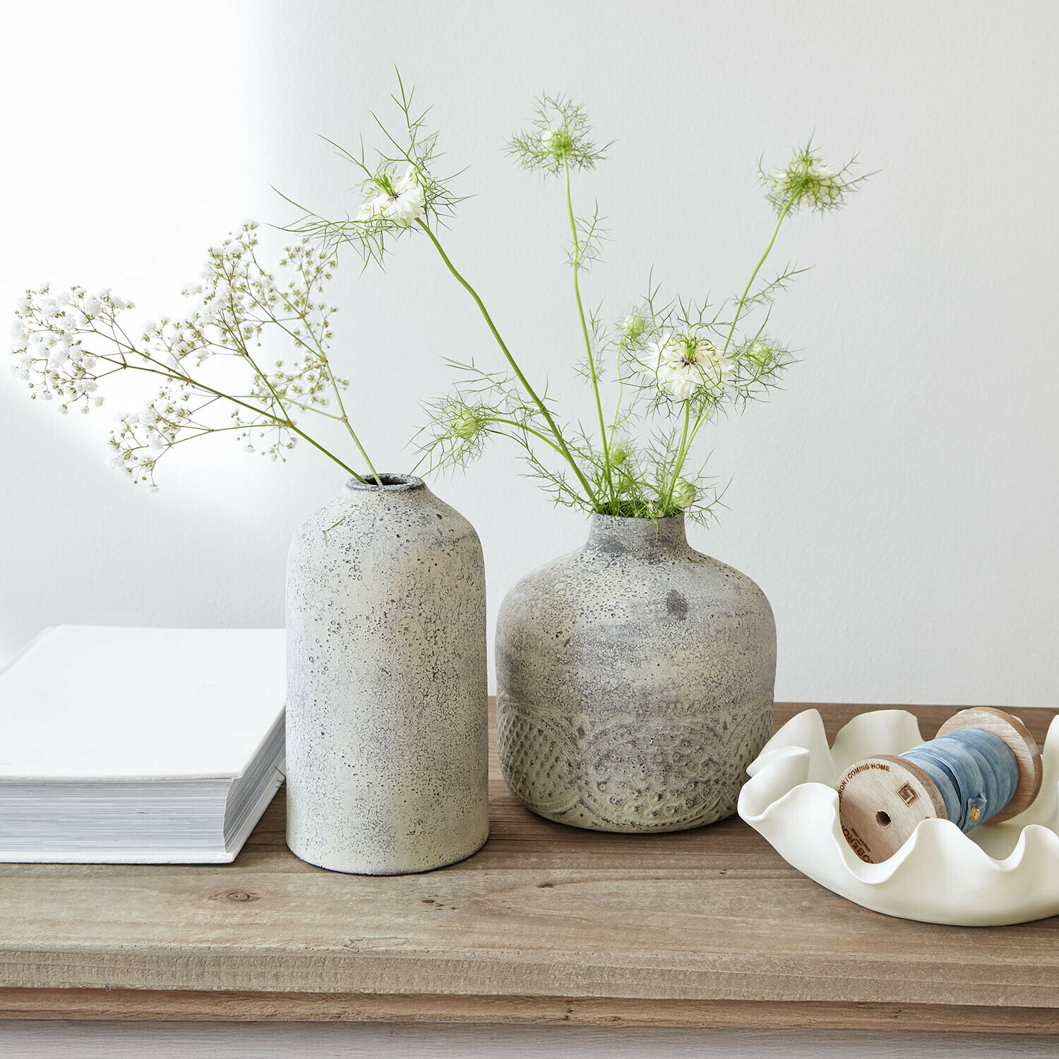 Twee grijze keramische vazen met fijne witte bloemen op een lichte houten tafel