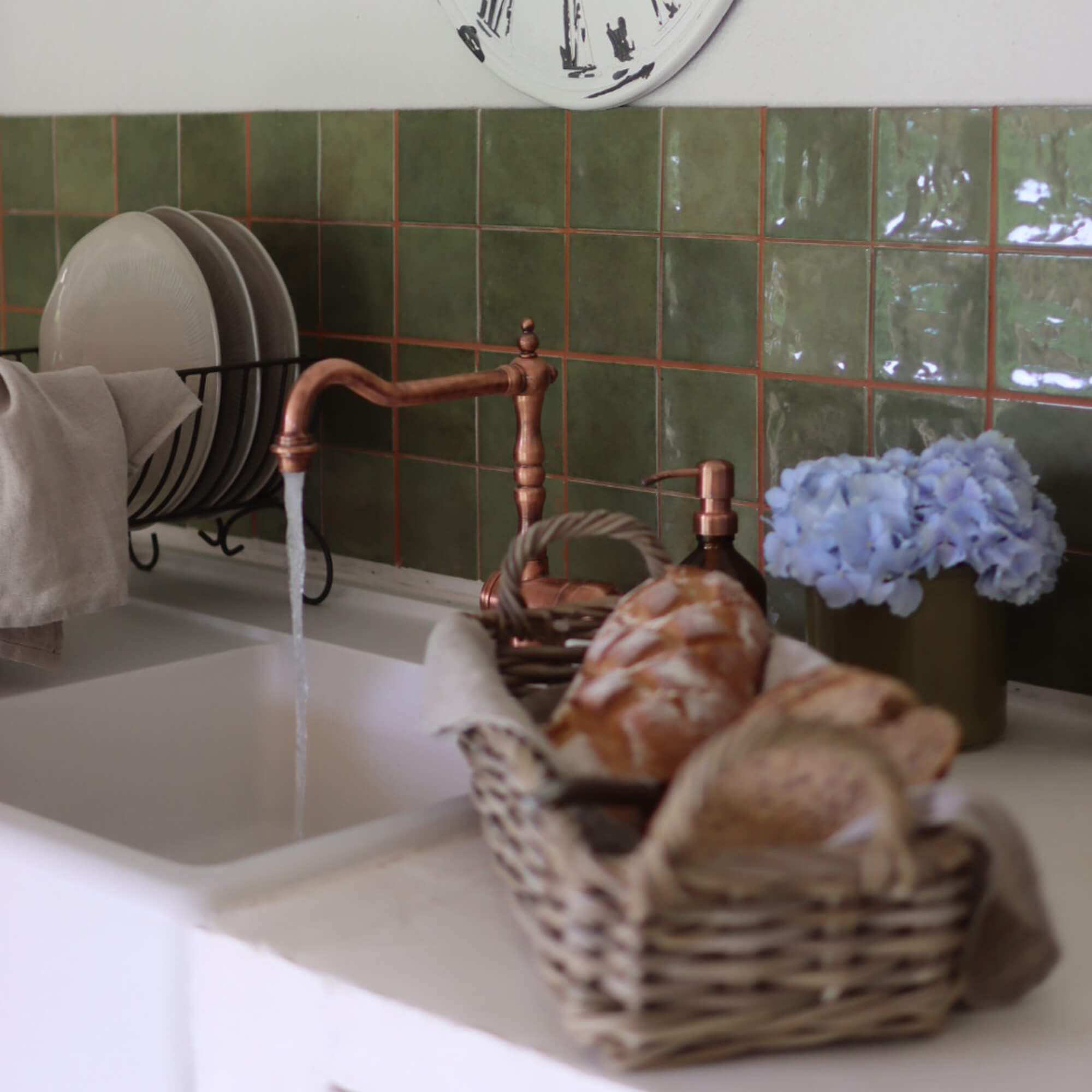 Keuken met koperen kraan, groene tegels, broodmand en blauwe bloemen als decoratie