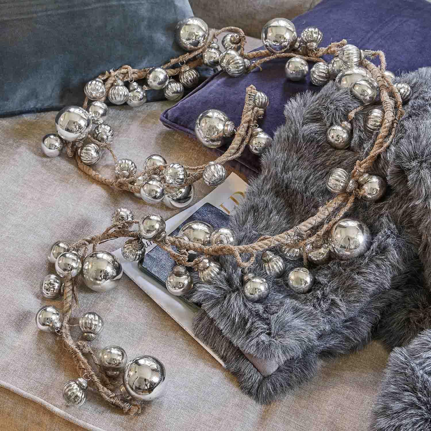 Decoratieve ketting met zilverkleurige metalen ballen aan juten touw op zachte kussens en bont