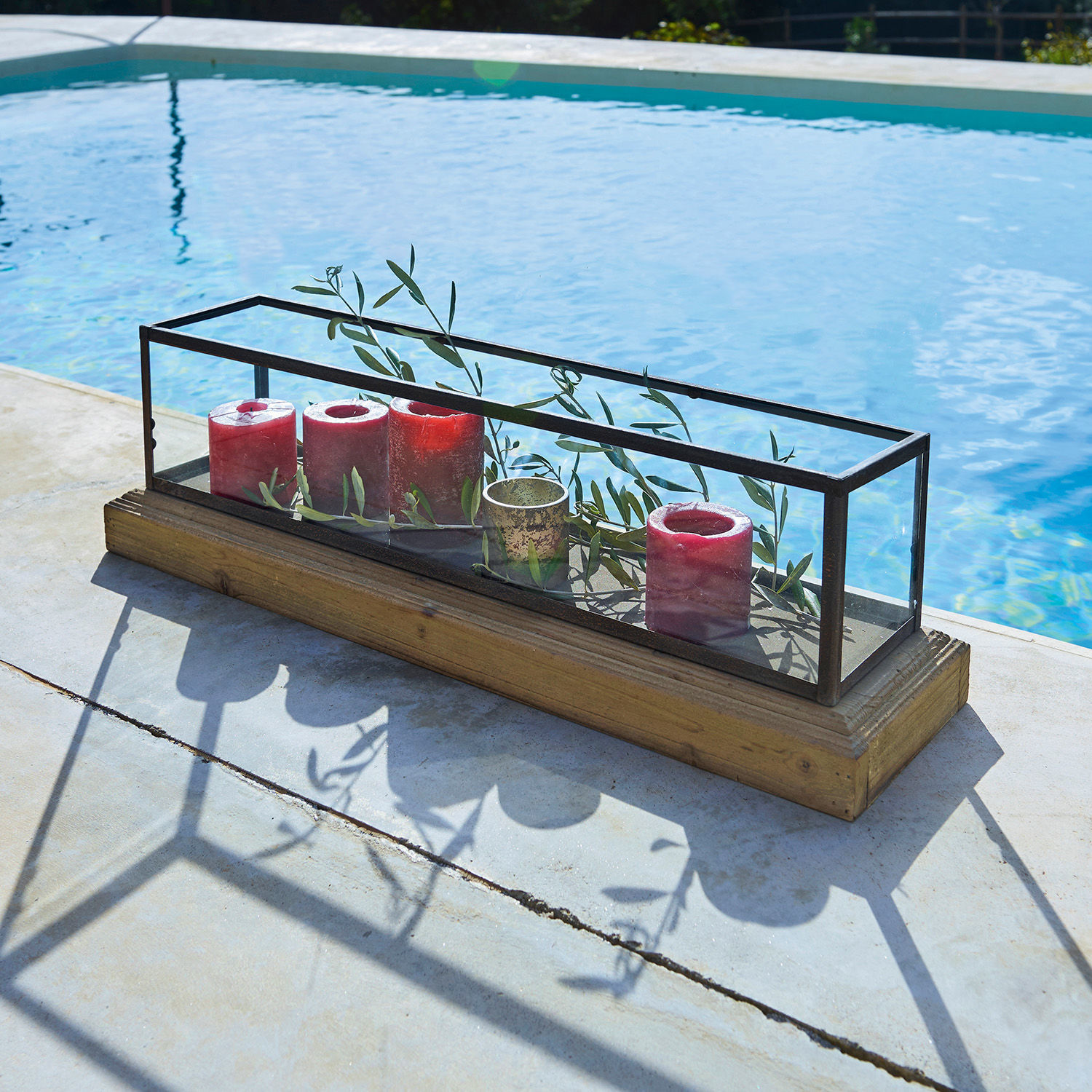 Glazen decoratie met metalen frame en houten voet, rode kaarsen en groene takken binnenin