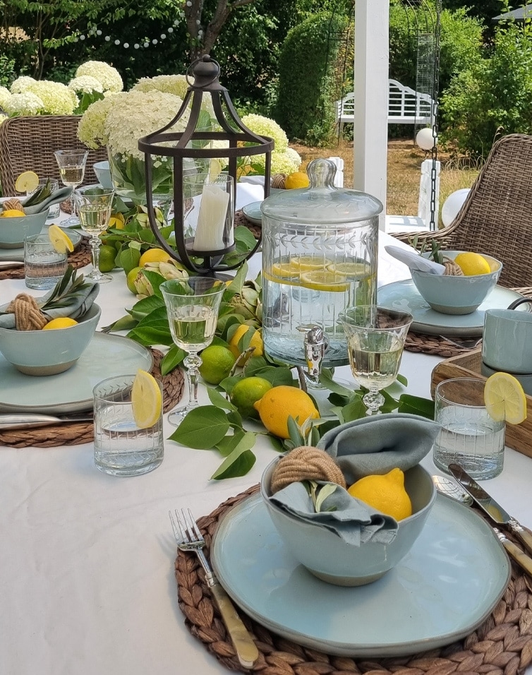 Zomerse buitentafel met blauw servies, citroenen en glazen waterdispenser met citroen