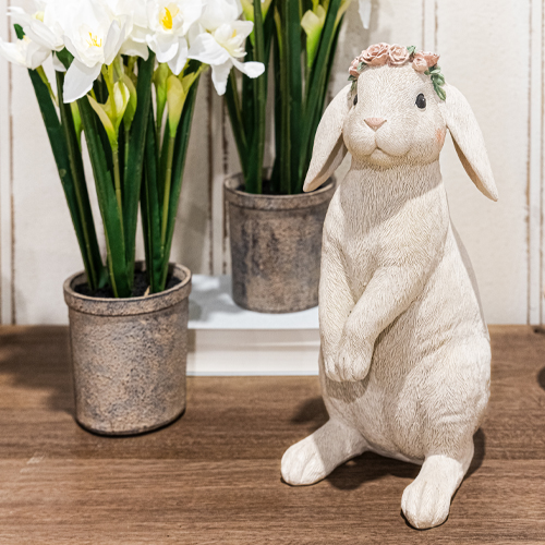Decoratief wit konijn met bloemenkrans op houten tafel naast potten met witte bloemen