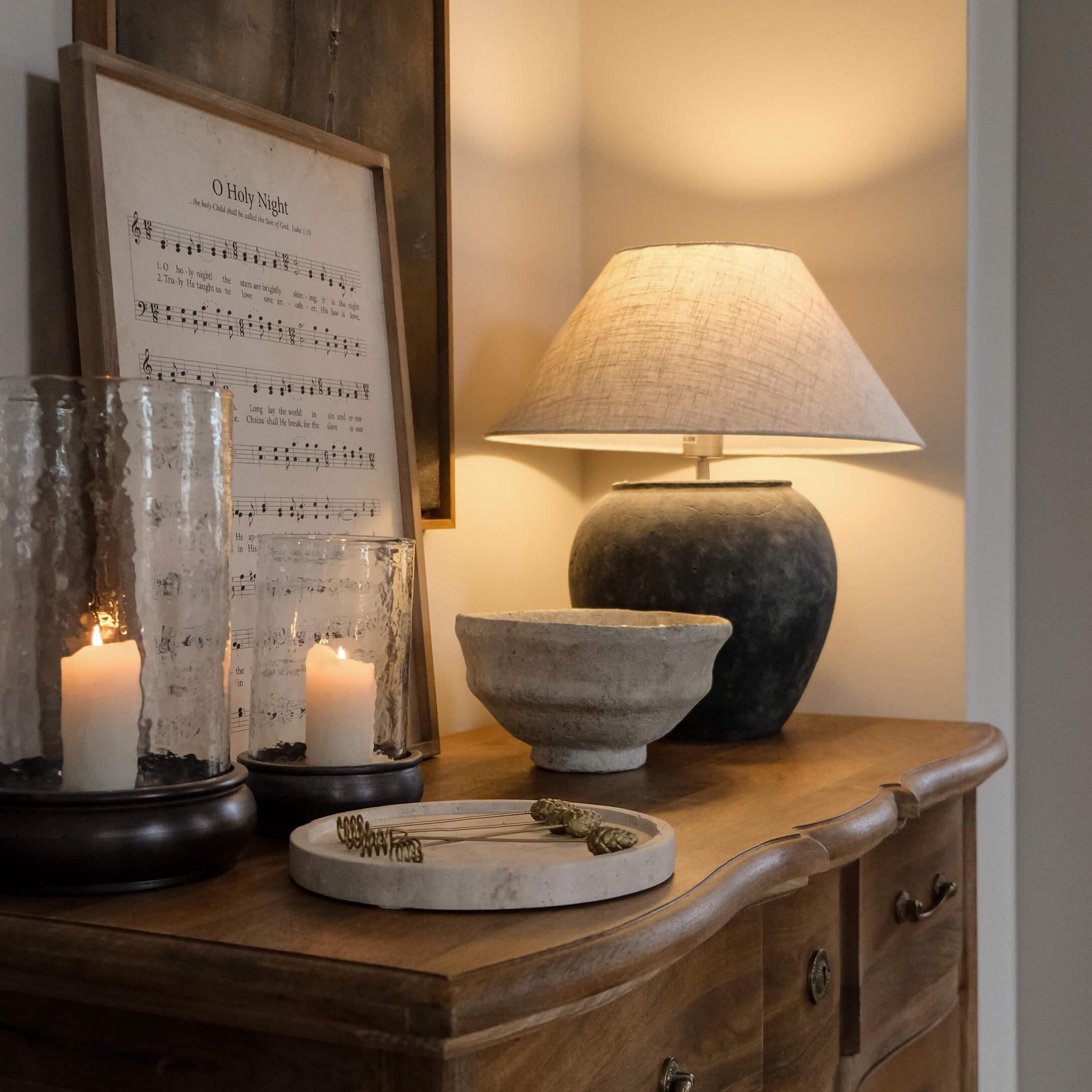 Tafellamp met zwarte keramische voet en beige kap op houten dressoir met decoraties