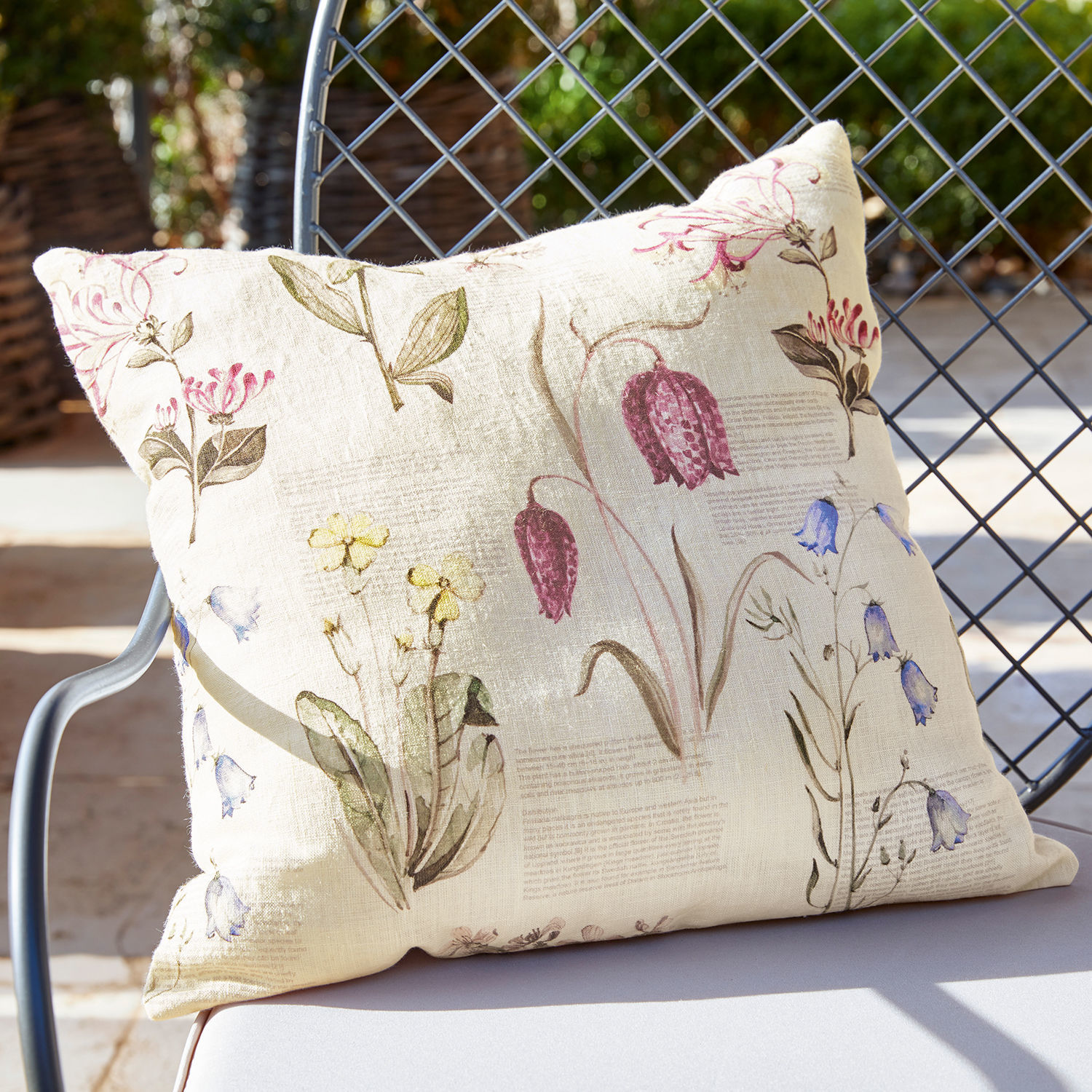 Kussenhoes Fournier Beige linnen kussen met vintage bloemenprint op een tuinstoel in zonlicht