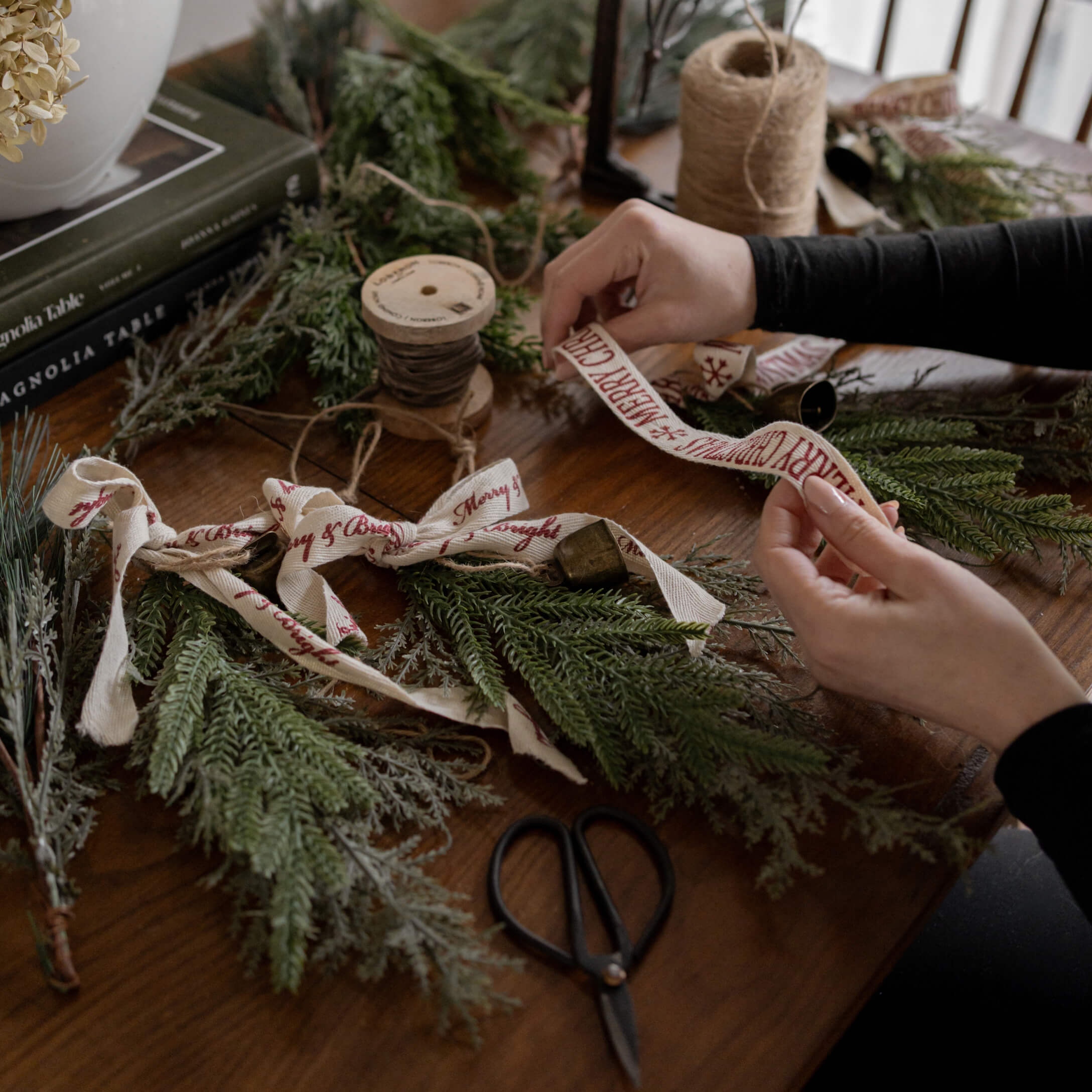 Handen die groene dennentakken versieren met katoenen lint Merry Christmas op houten tafel met schaar