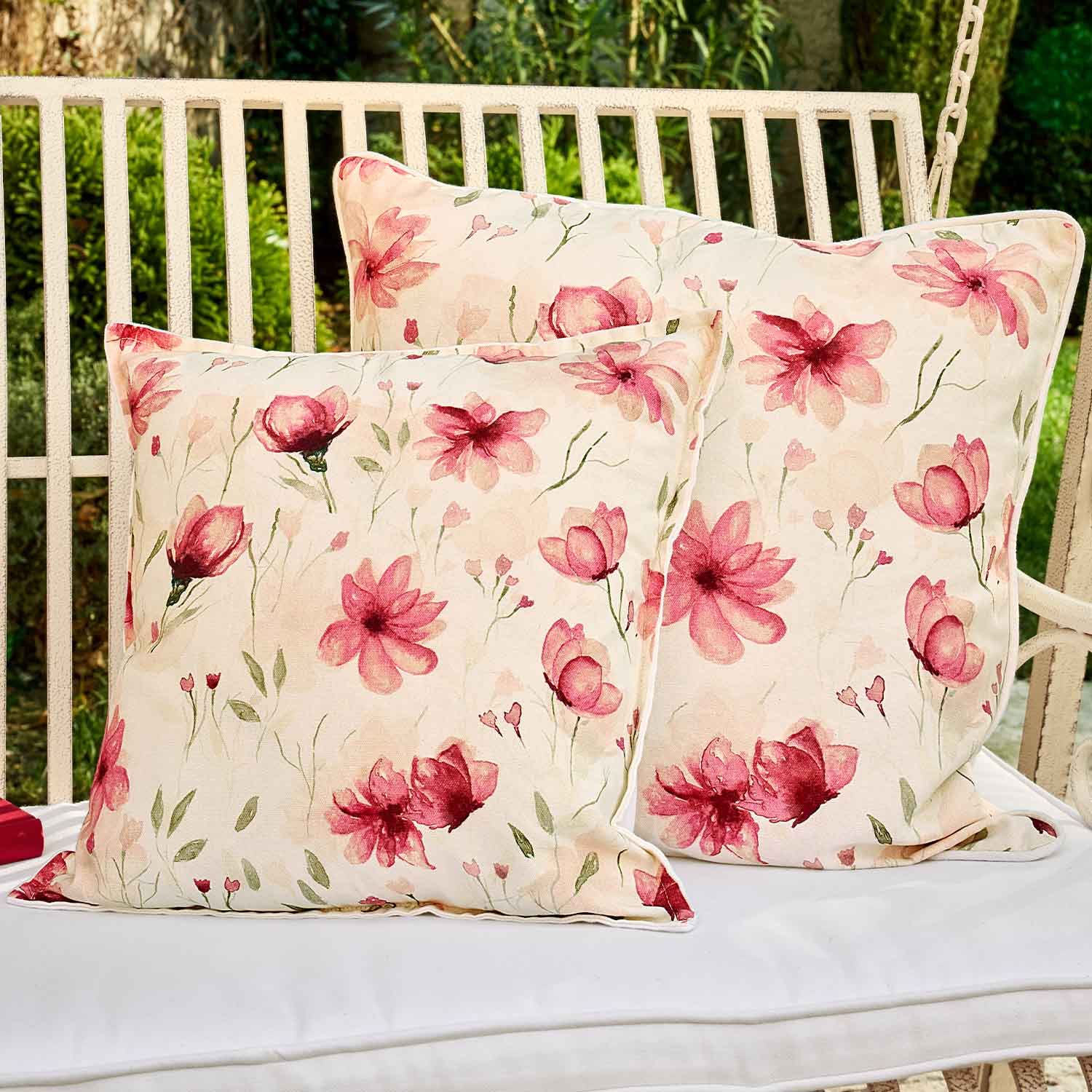 Twee vierkante katoenen kussens in crèmekleur met roze bloemen, perfect voor tuinmeubilair