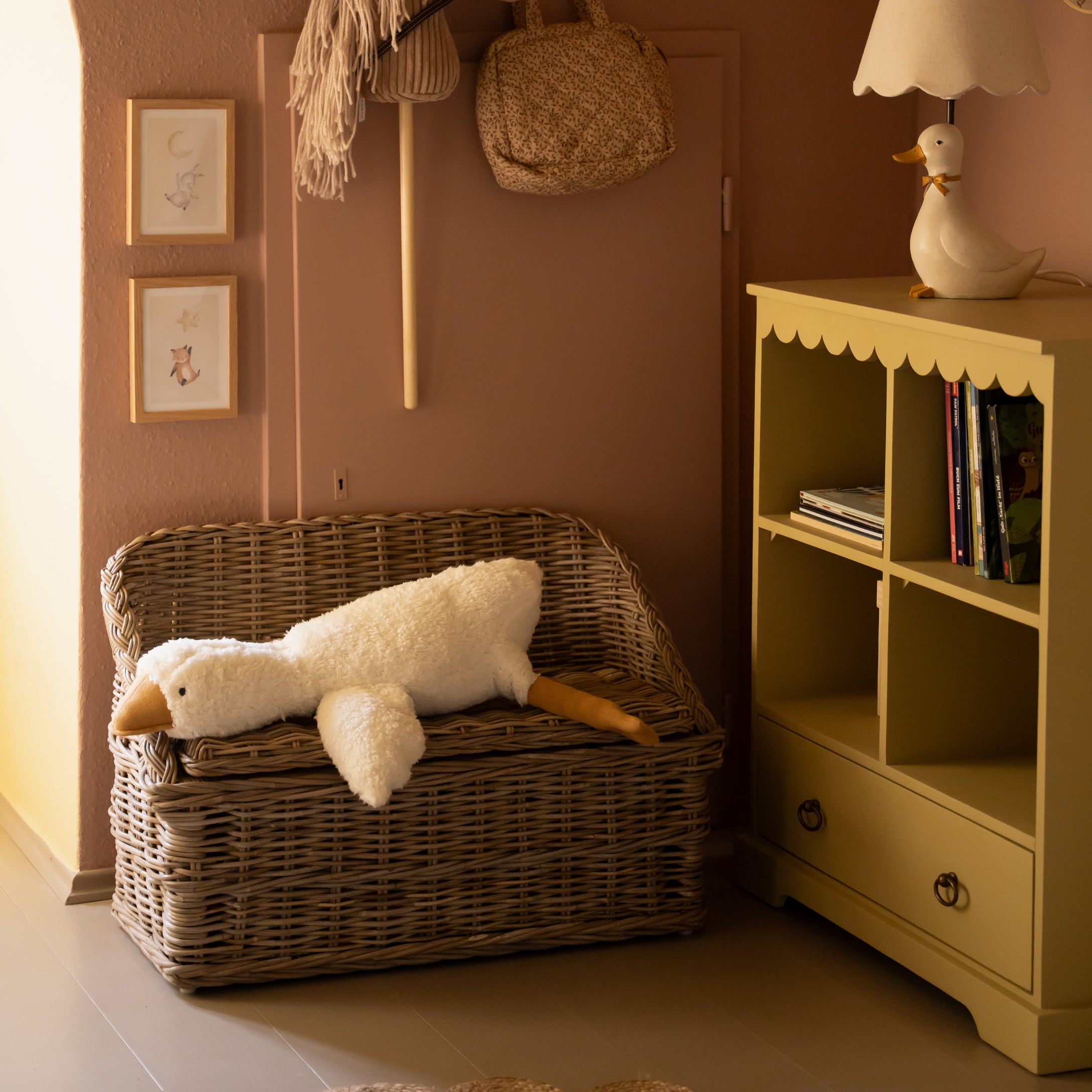 Rotan bank met lange witte pluche eend knuffel in gezellige kinderkamer met gele kast