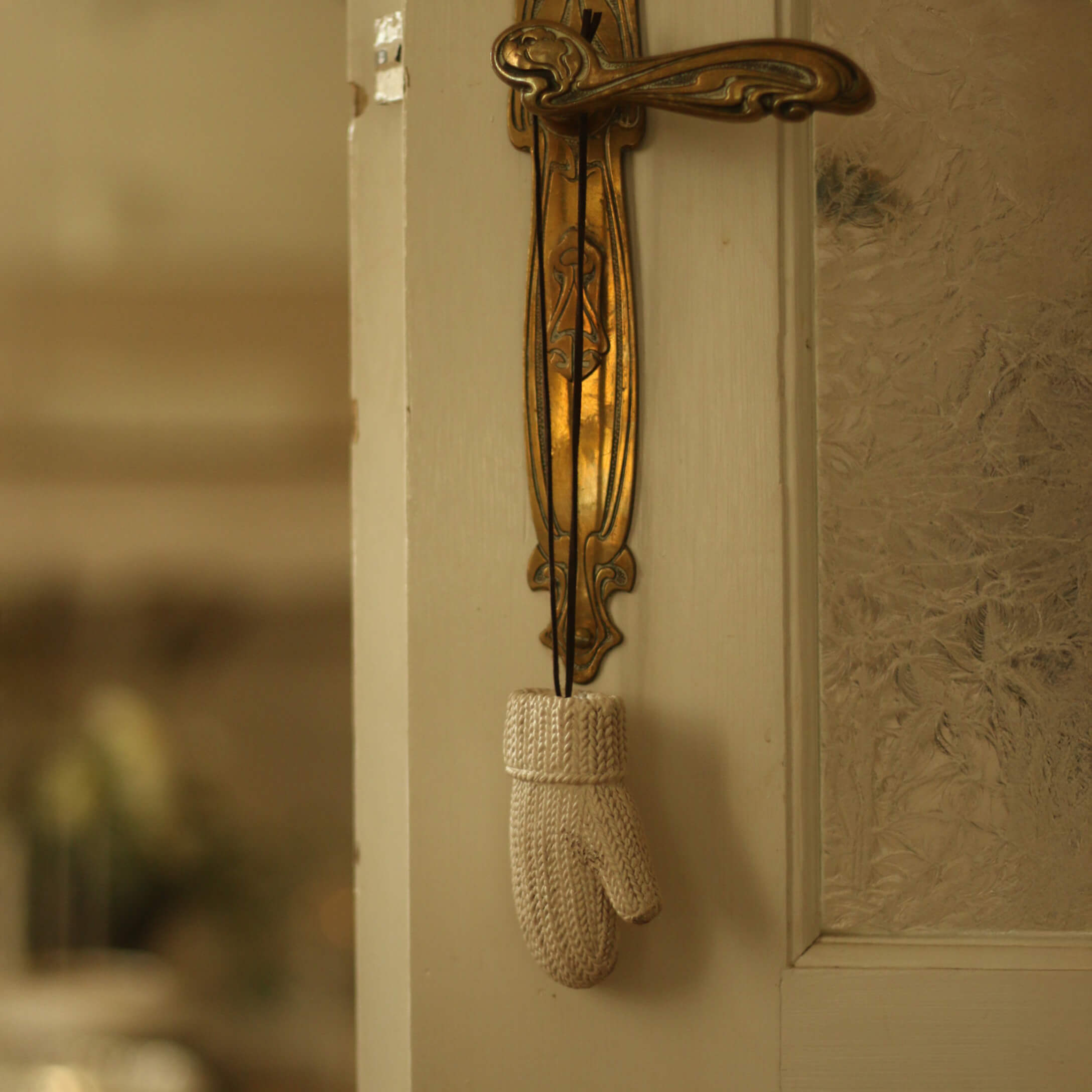 Witte gebreide decoratieve want hangend aan een gouden messing deurklink