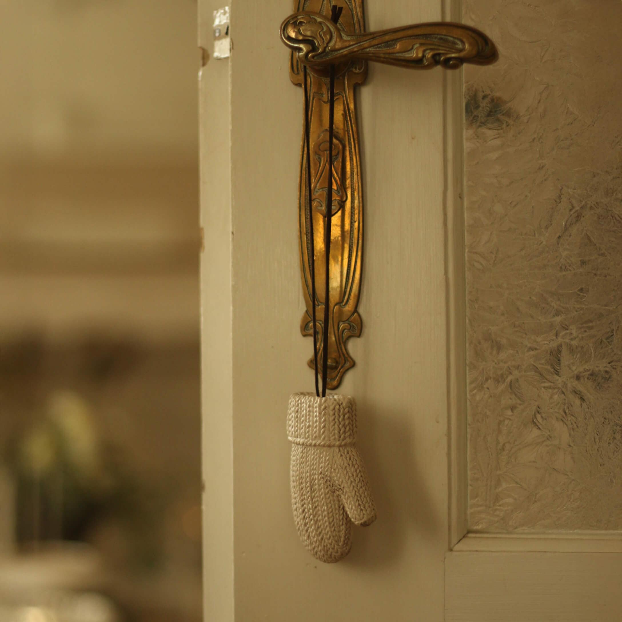 Witte gebreide decoratieve want hangend aan een gouden messing deurklink