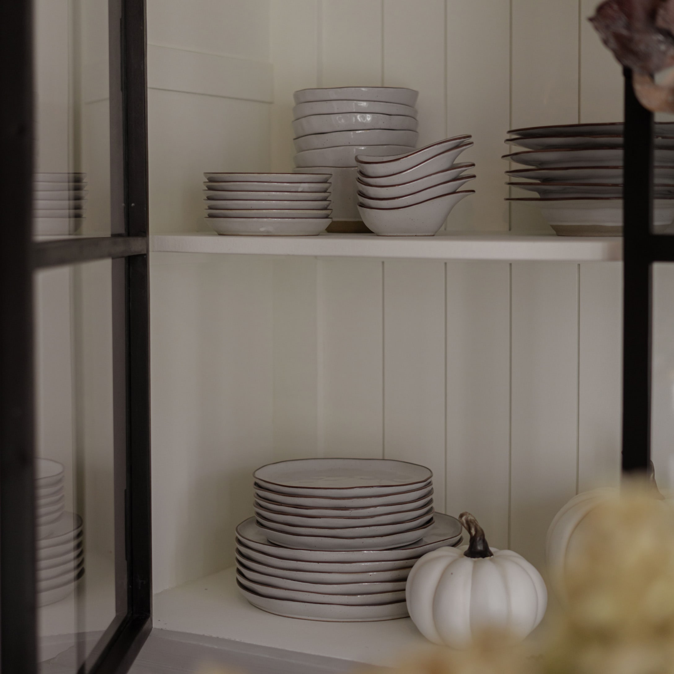 Set wit keramiek met bruine rand op plank, decoratieve witte pompoen ernaast, rustieke stijl