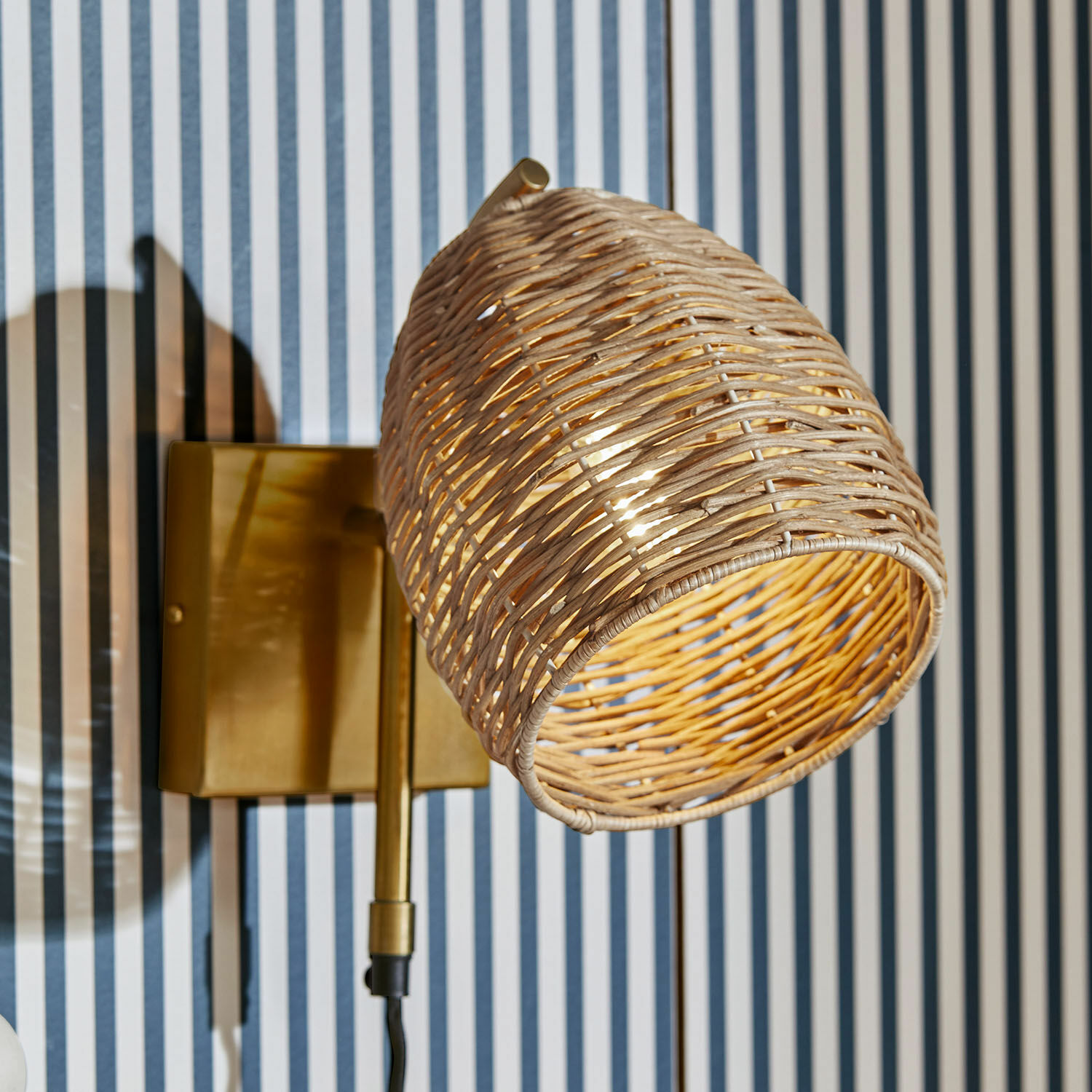 Wandlamp Anglemont Wandlamp met gevlochten rotan kap en messing basis tegen gestreepte muur