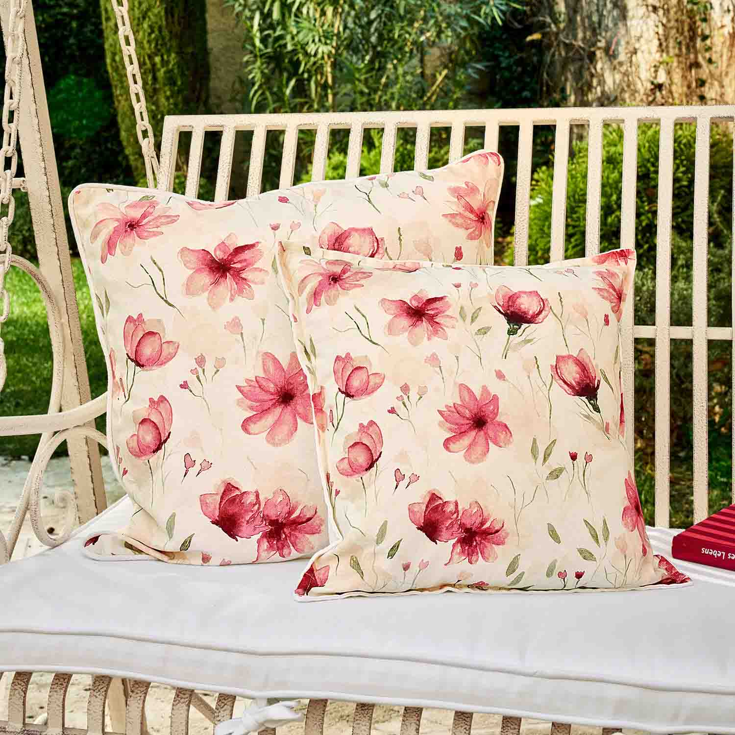 Twee decoratieve katoenen kussens in crème met roze bloemen op een metalen tuinschommel