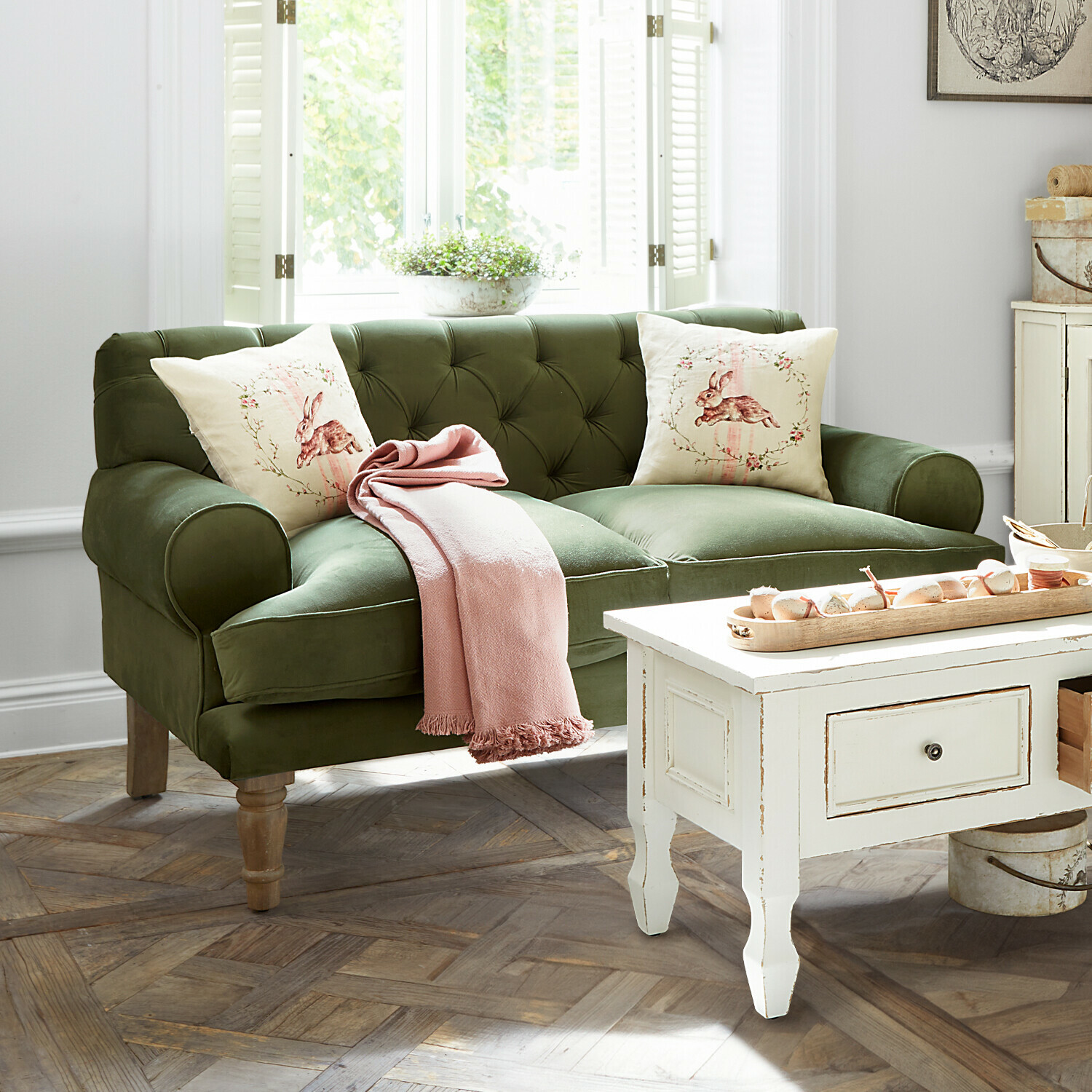 Groene fluwelen bank met kussens met konijnmotief en roze deken in lichte woonkamer