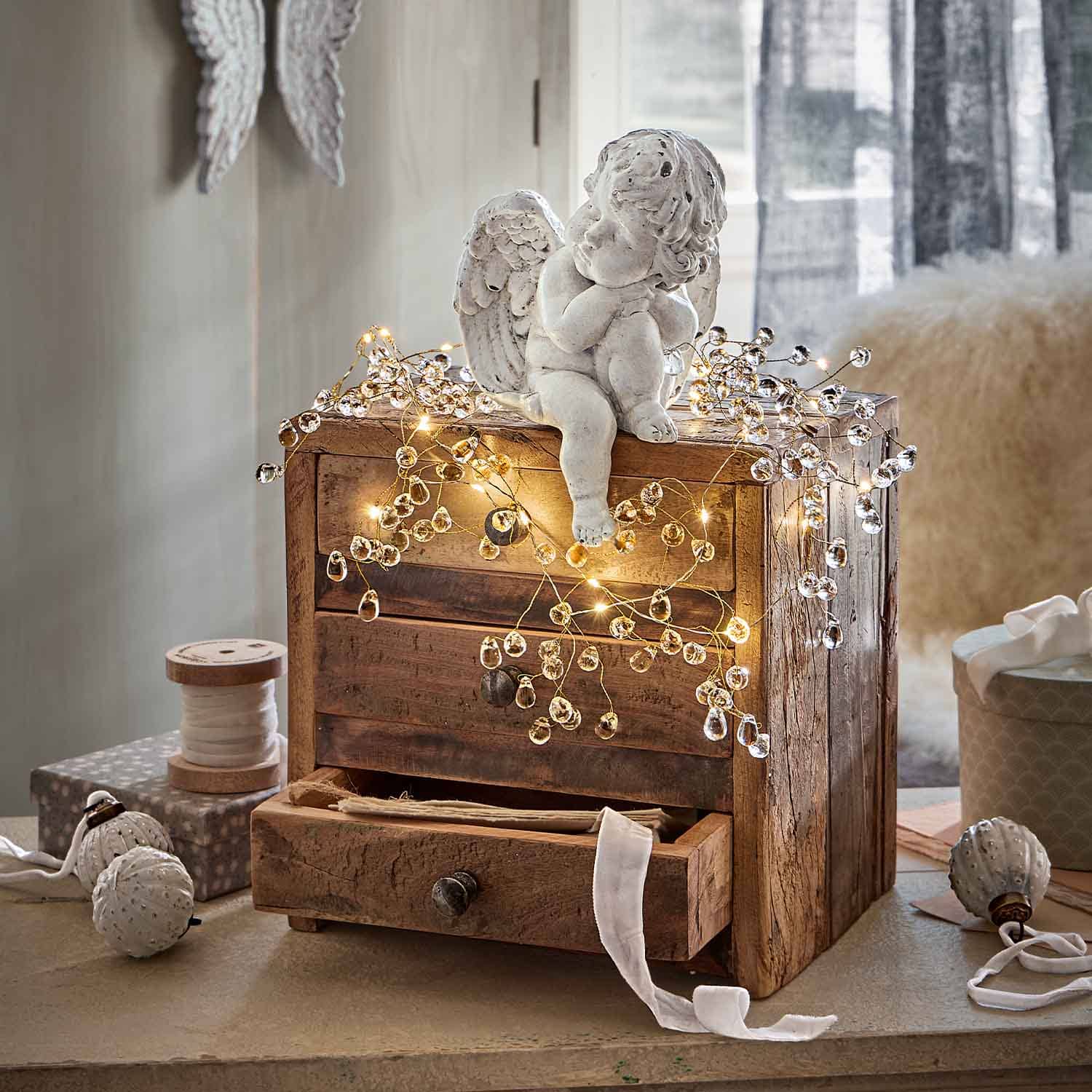 Witte keramische engel op houten kist versierd met warme LED-lichtjes