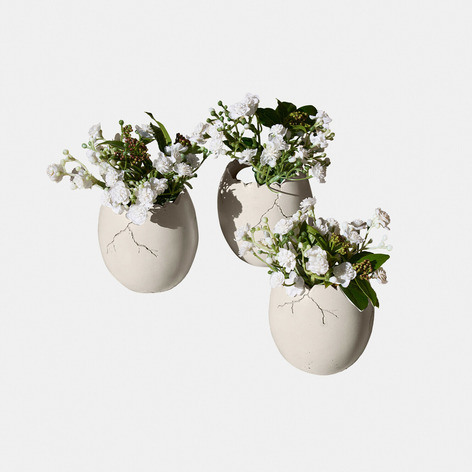Decoratief ei set van 3 Waverlye Drie witte keramische eivormige vazen met witte bloemen en groene bladeren als decoratie.