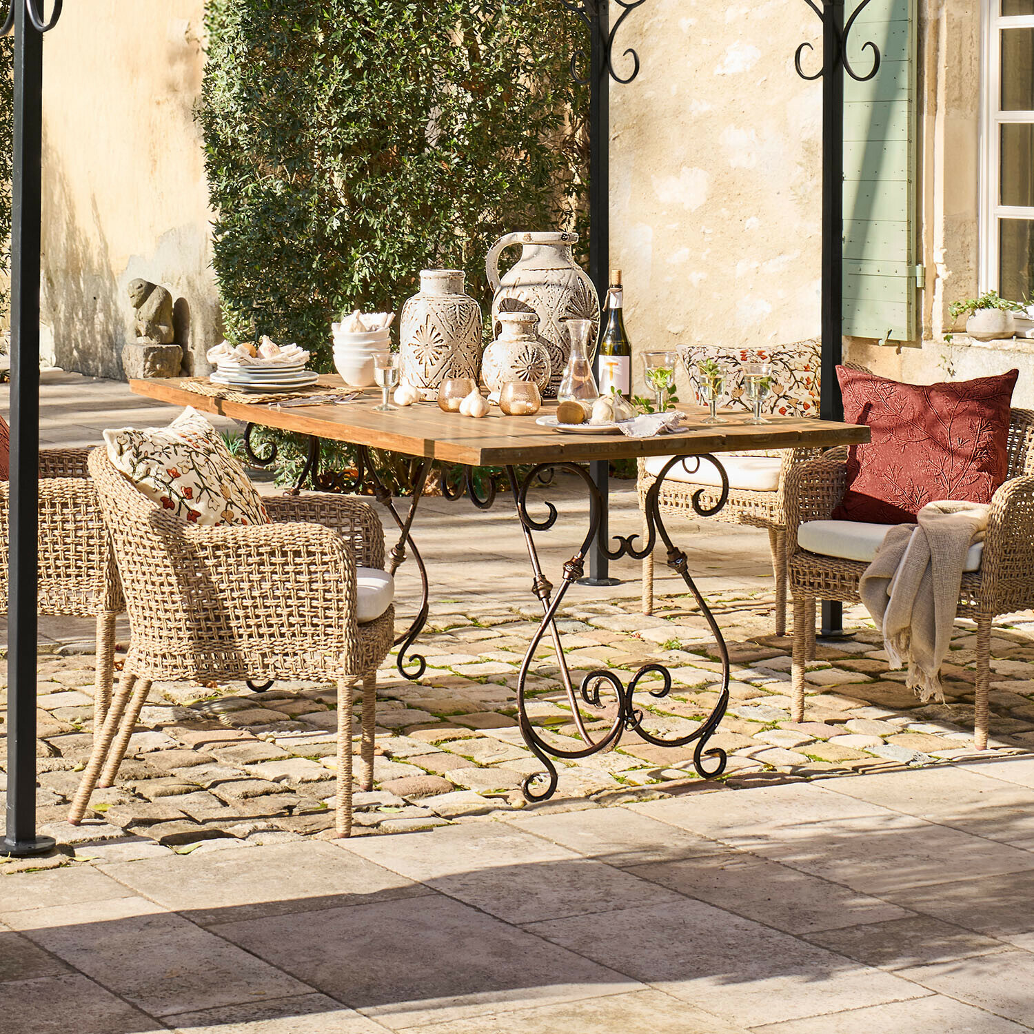 Tuin tafel met houten blad en metalen poten, rieten stoelen met kussens en keramische decoraties