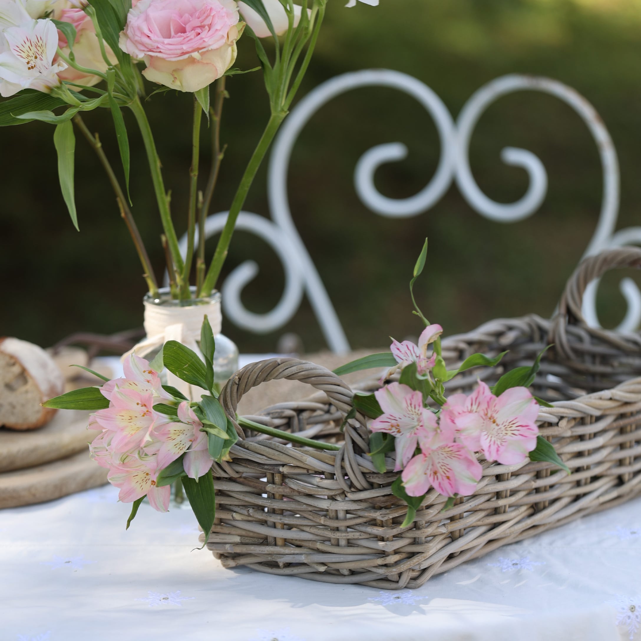 Rustieke mand van natuurlijk riet met roze bloemen op een wit tafelkleed in de tuin