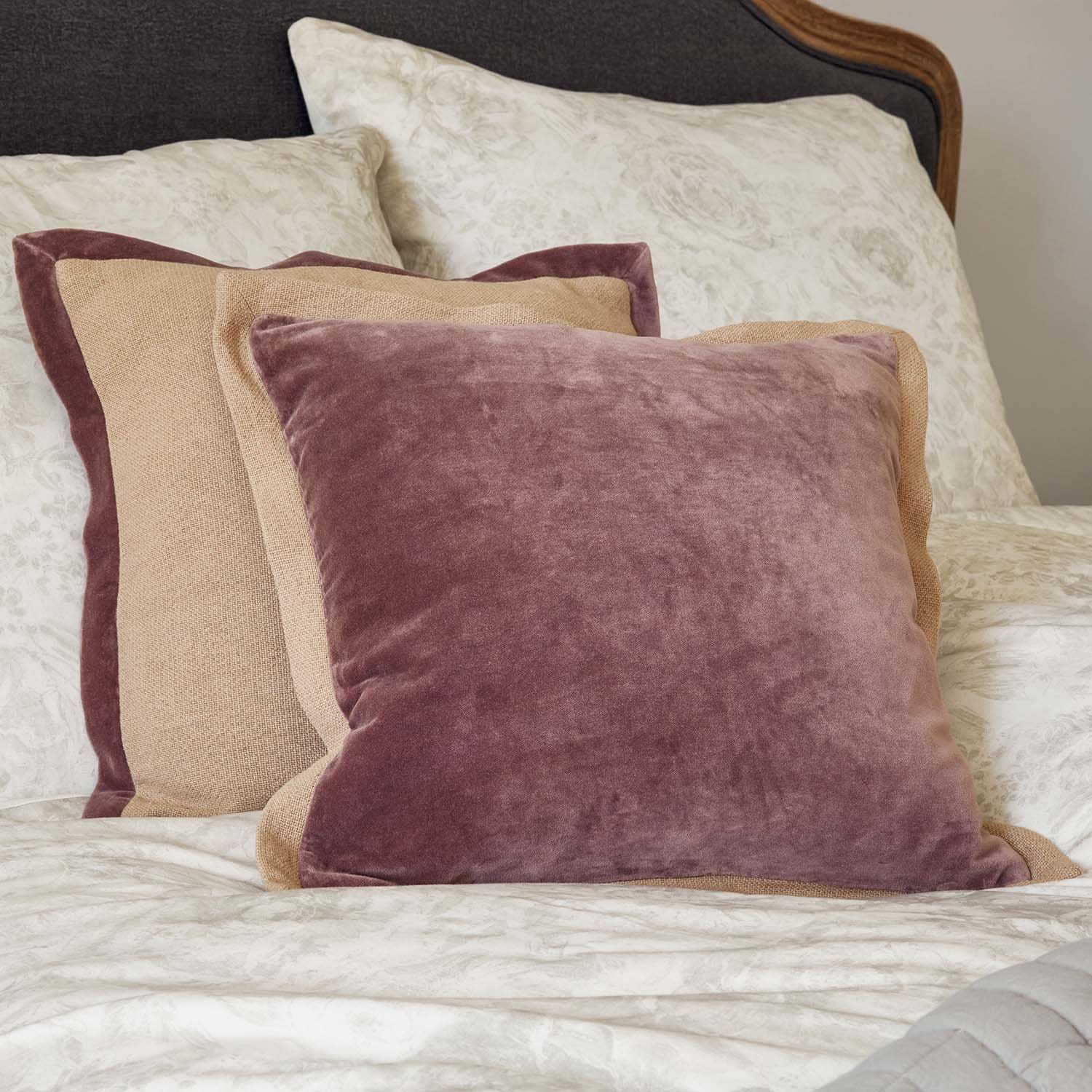 Set decoratieve kussens van fluweel en linnen in roze en beige op een bed met bloemenpatroon