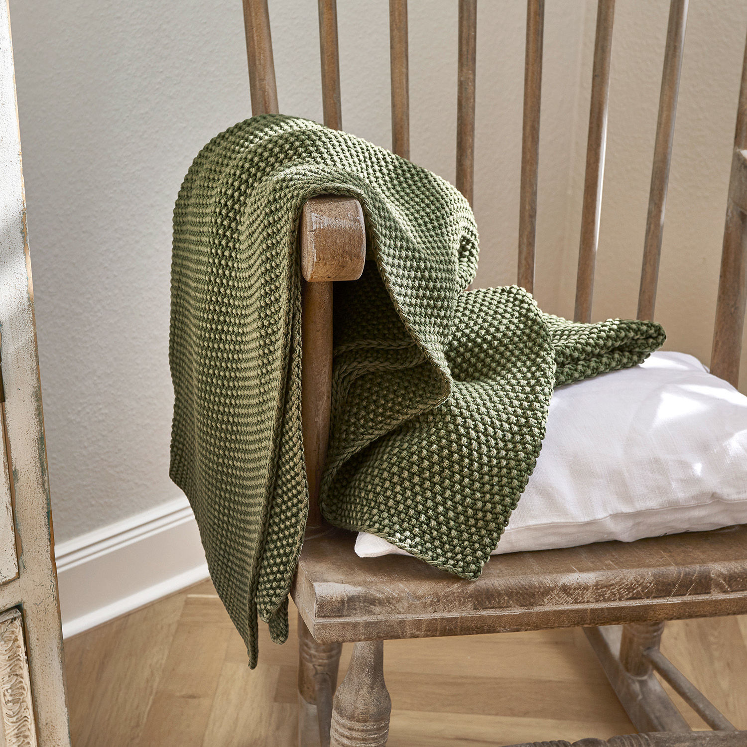 Plaid Amberley Groene gebreide katoenen deken op houten stoel met wit kussen, sfeervolle interieurdecoratie