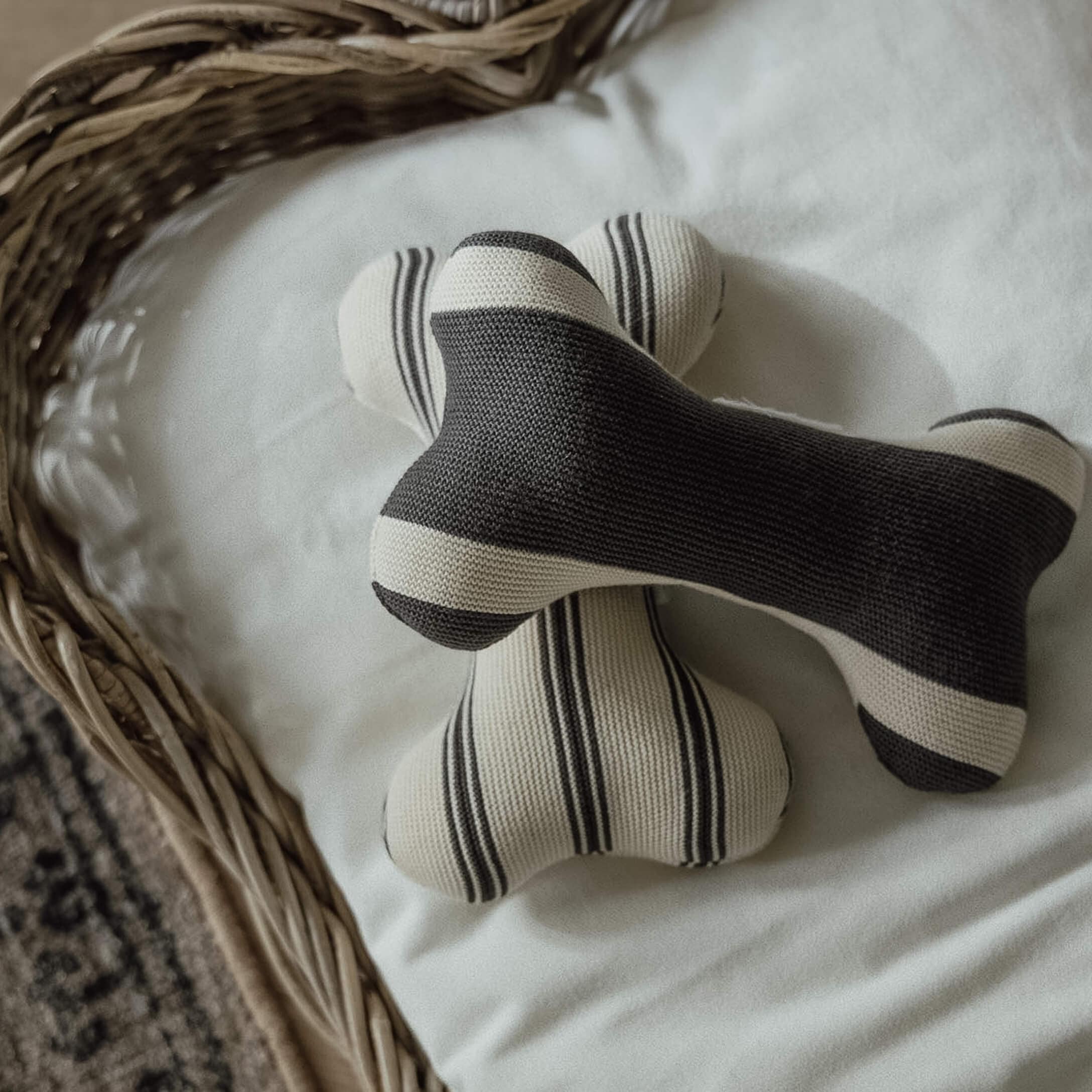 Twee gebreide botvormige speeltjes met zwart-witte strepen op witte achtergrond in een rieten mand