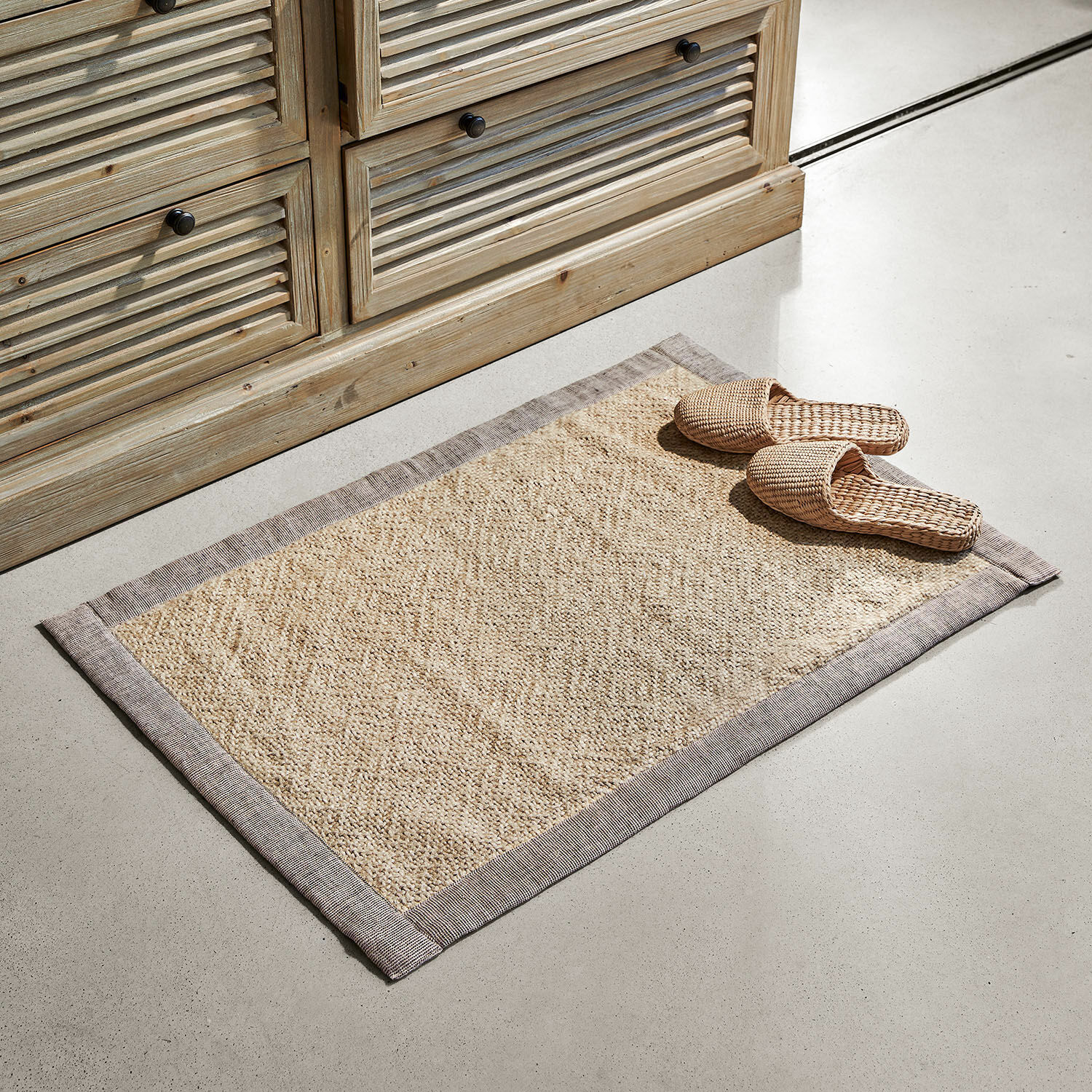 Badmat Wilder Beige vloerkleed van natuurlijk materiaal met grijze rand op lichte vloer naast houten kast