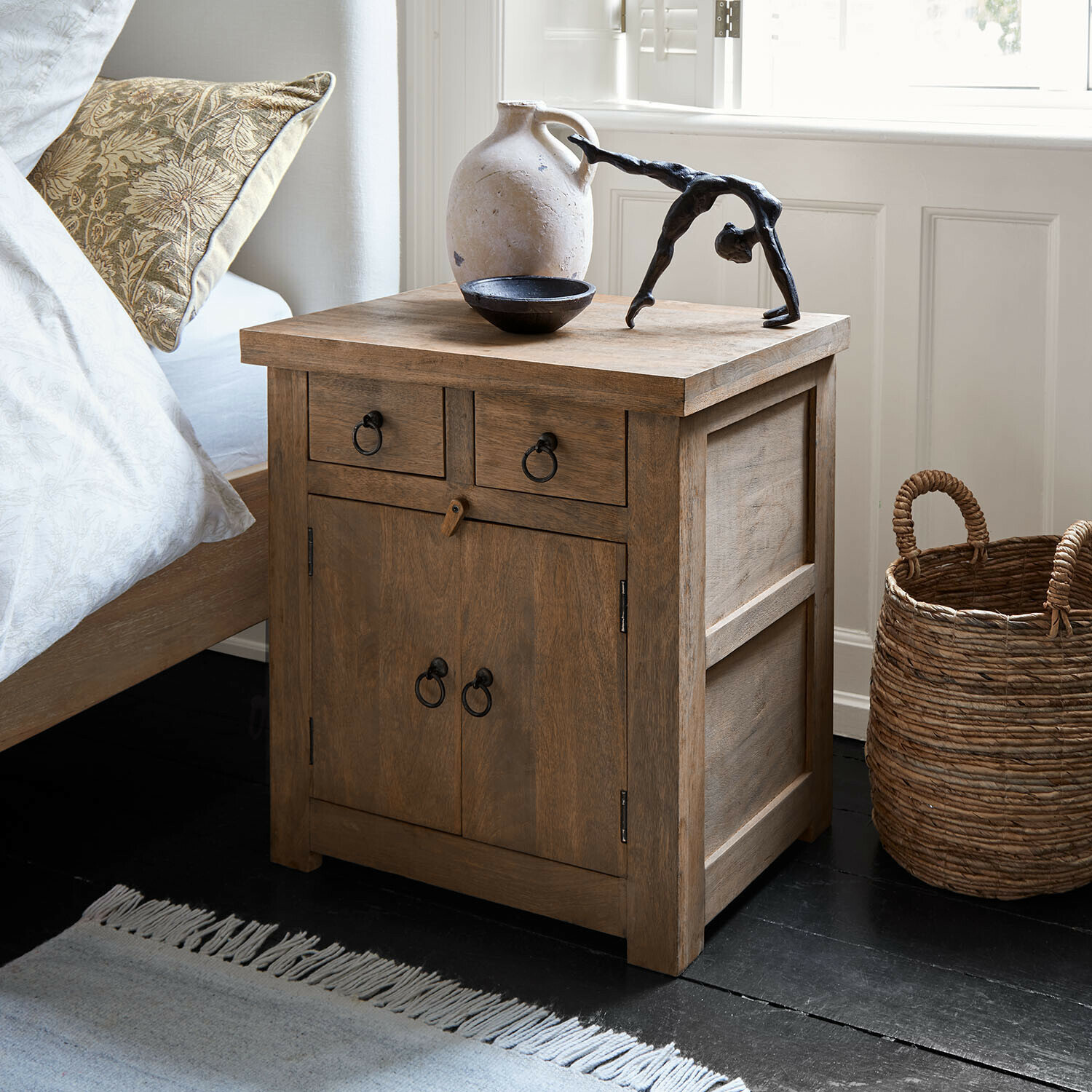 Nachtkastje van natuurlijk hout met metalen handgrepen en decoratieve voorwerpen erop in slaapkamer