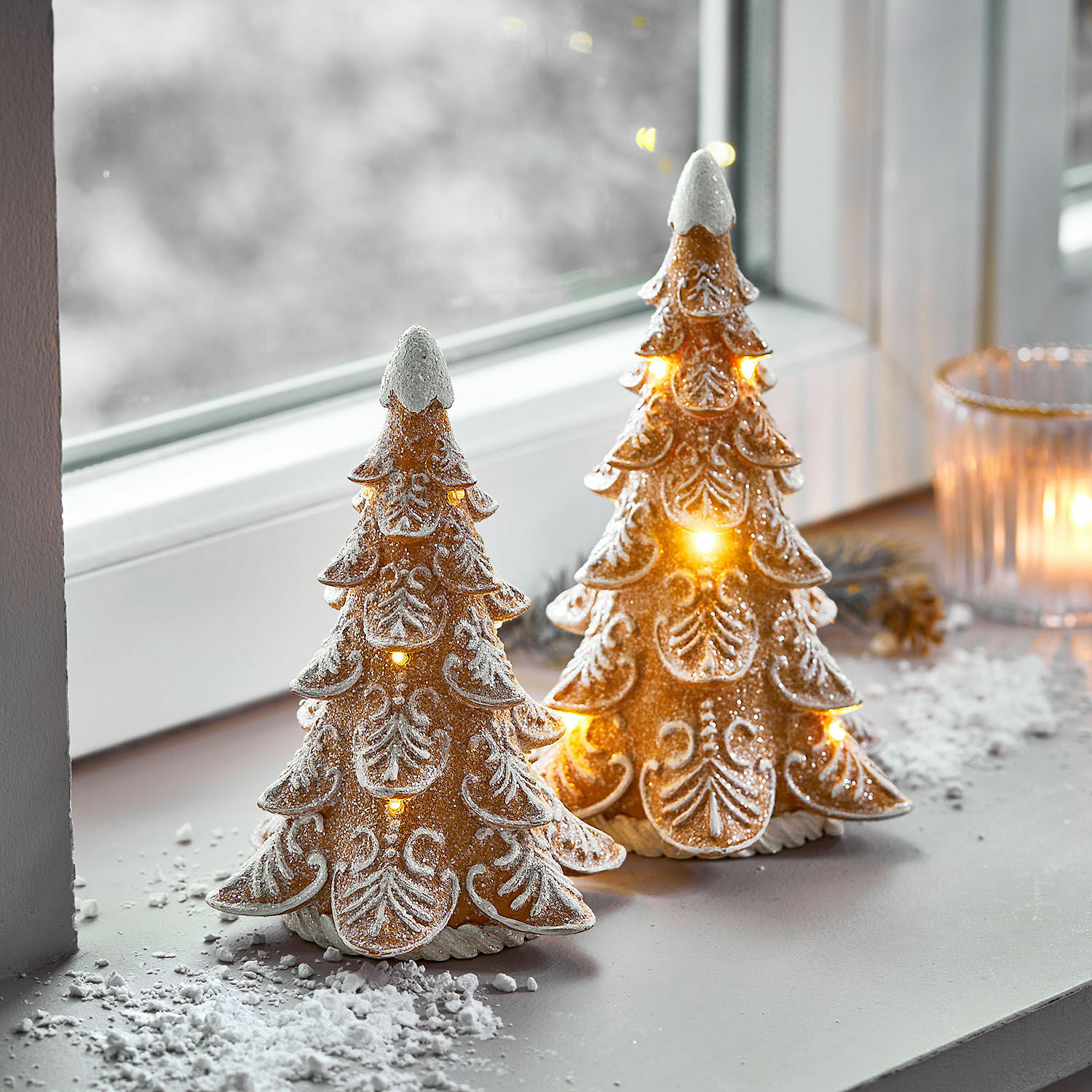 Twee decoratieve keramische kerstbomen met LED-verlichting en wit sneeuw effect op vensterbank