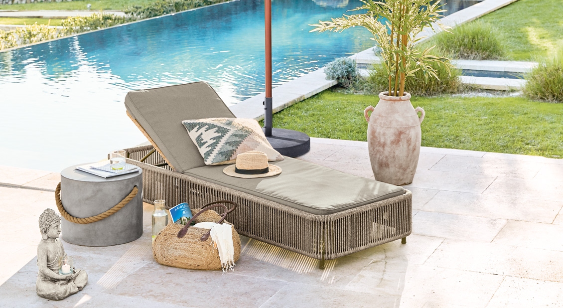 Tuinligstoel met beige kussen en sierkussen bij zwembad op lichte stenen terras met natuurlijke decoratie