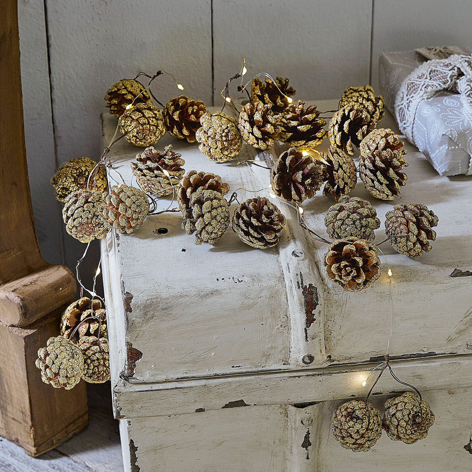Lichtsnoer Bannet Guirlande van natuurlijke dennenappels met glitters en subtiele LED-verlichting op wit houten meubel