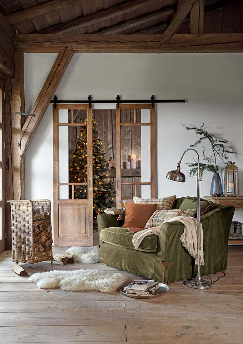 Gezellige woonkamer met groene bank, houten schuifdeuren en versierde kerstboom op de achtergrond