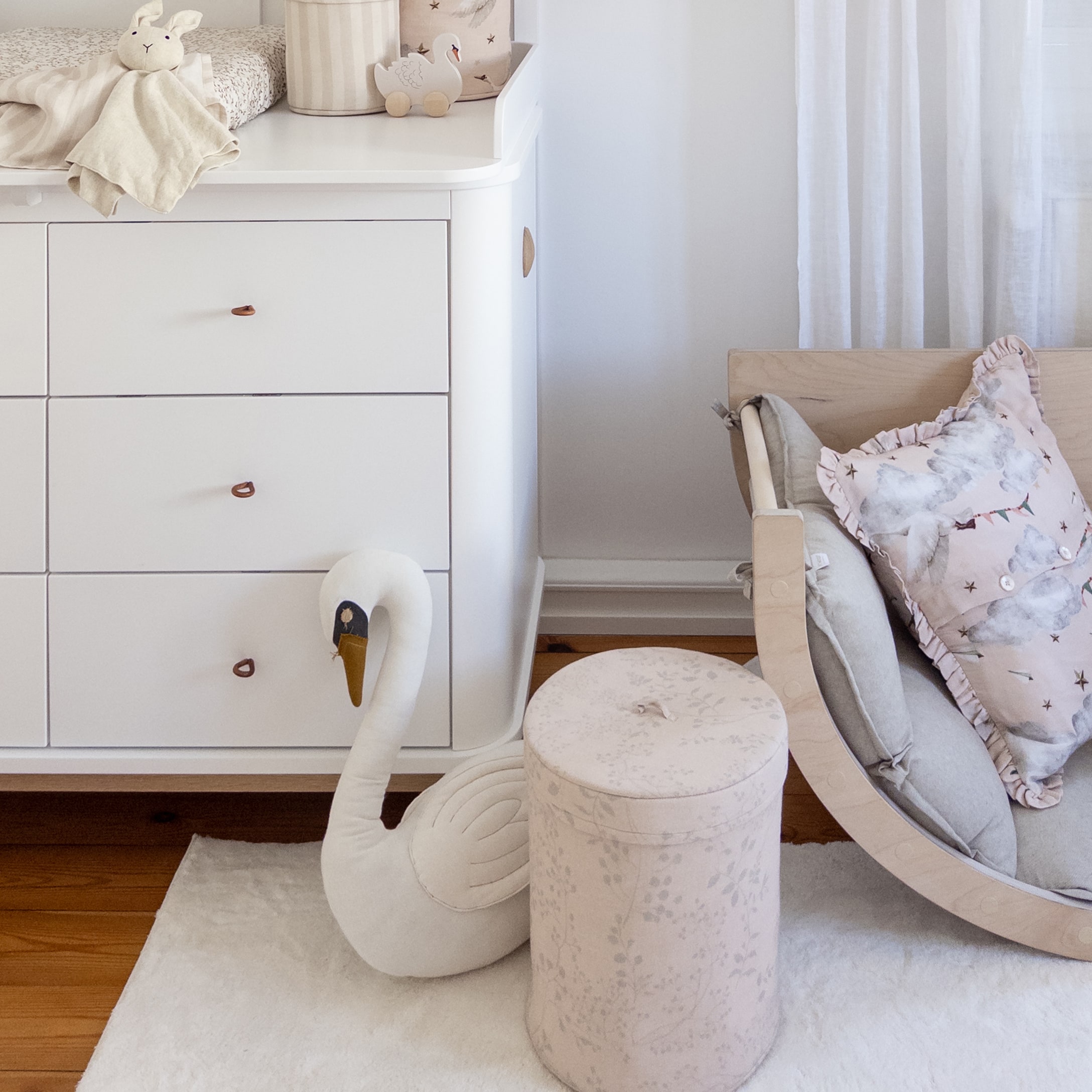 Gezellige kinderkamer met witte ladekast, pluche zwaan en roze stoffen poef