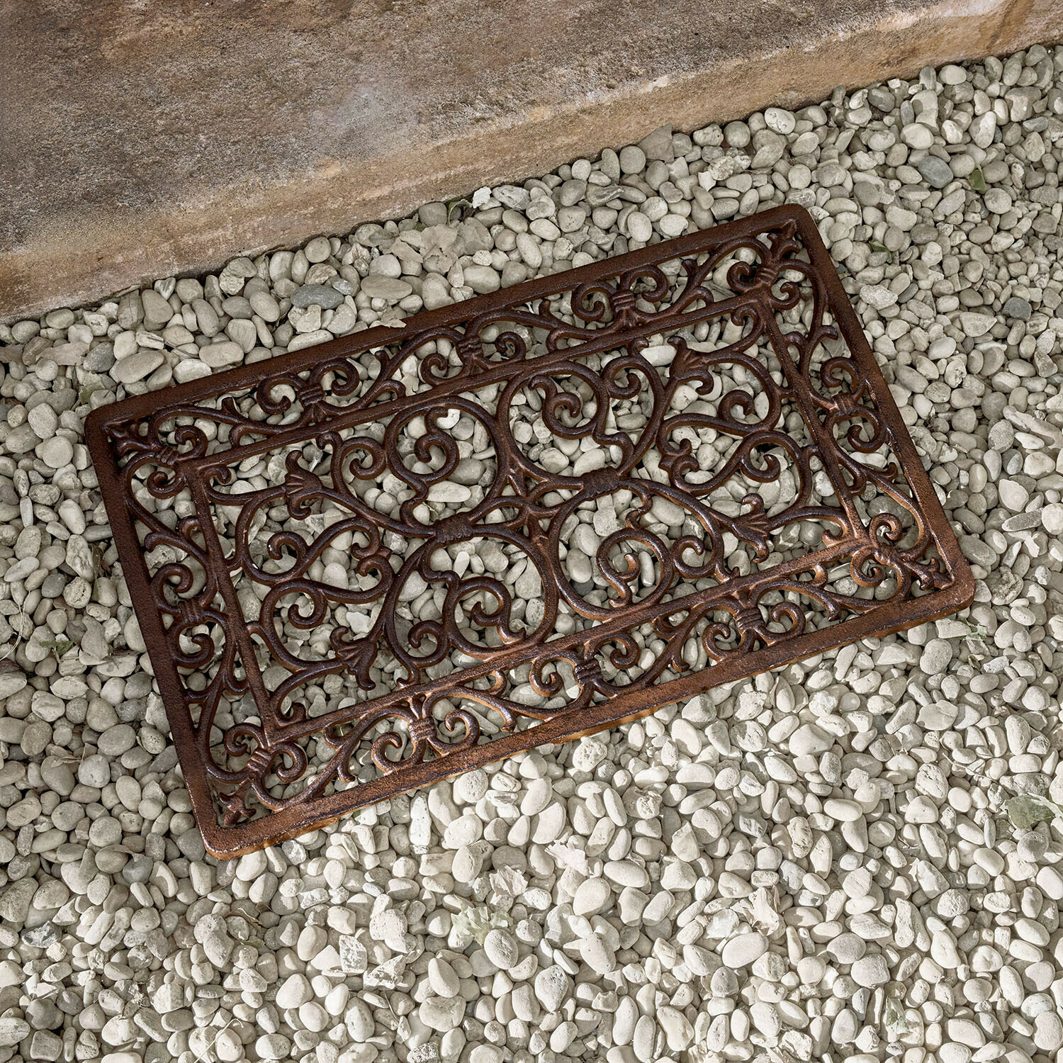 Bruine metalen mat met decoratief patroon op witte stenen, gietijzeren deurmat