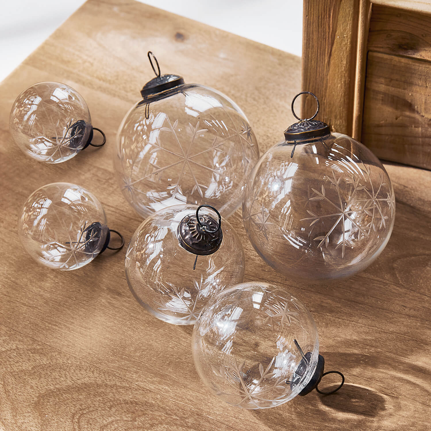 Transparante glazen kerstballen met gegraveerd sneeuwvlokpatroon op houten tafel, feestelijke decoratie
