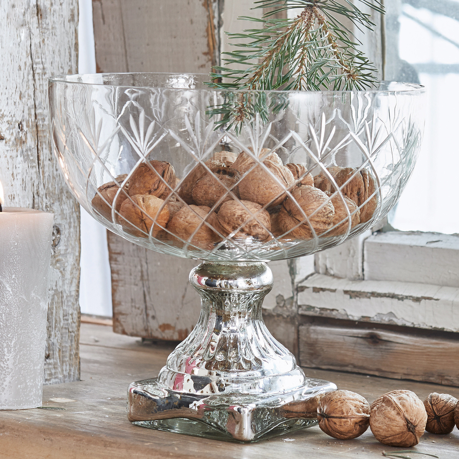 Glazen schaal op zilverkleurige metalen voet gevuld met noten op een rustieke houten tafel