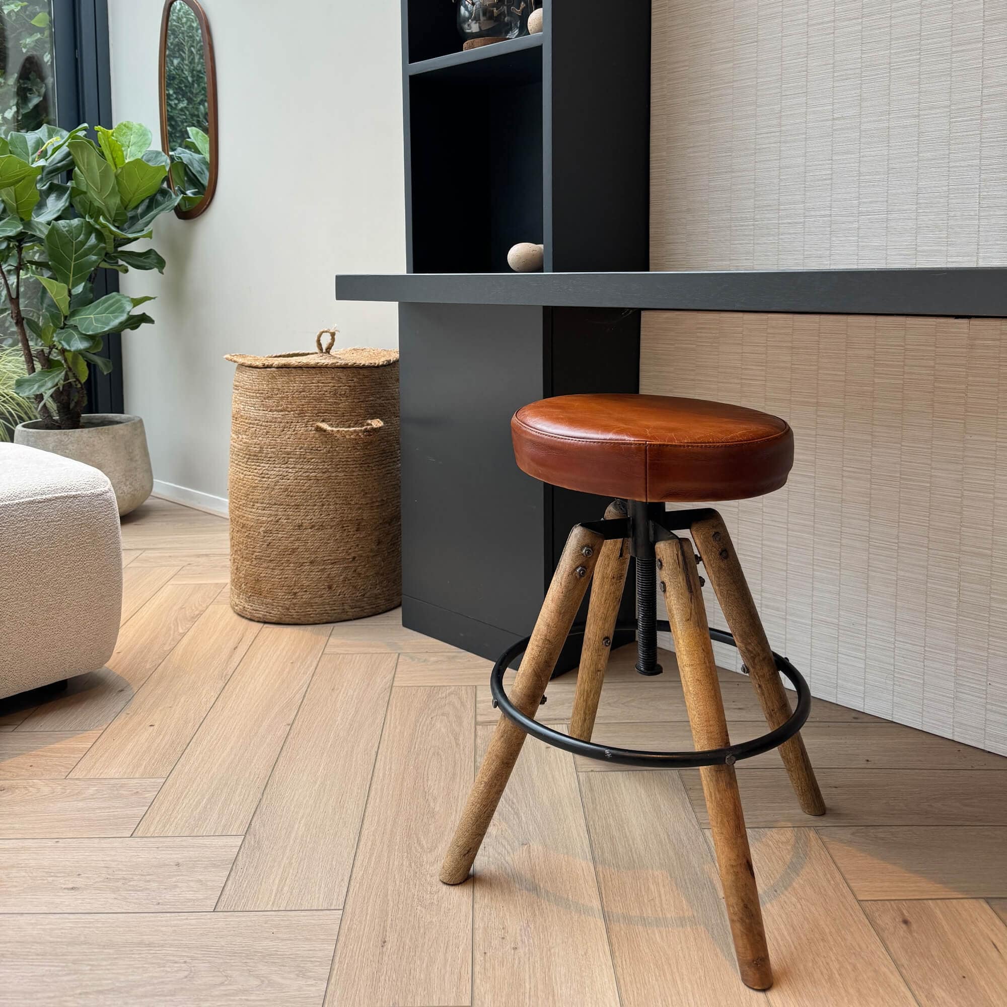 Barkruk met bruine leren zitting en houten poten op lichte houten vloer