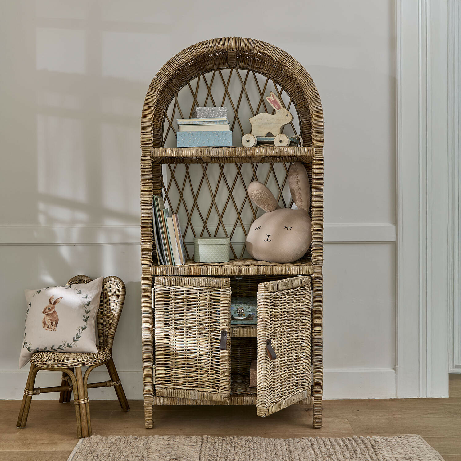 Rotan kast met afgeronde planken en kastje in natuurlijke kleur, kinderdecoratie en konijnen kussen