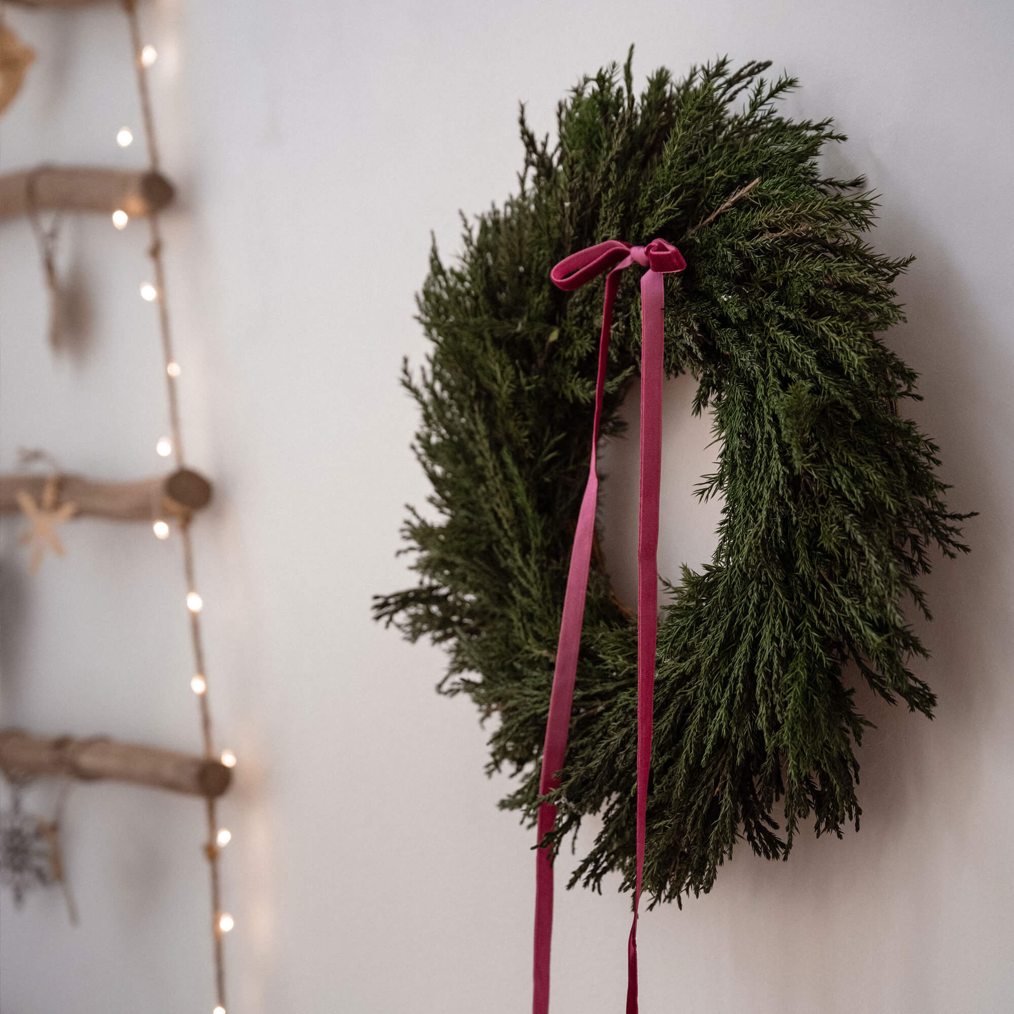 Groene kerstkrans met rode linten aan witte muur met decoratieve lichtjes