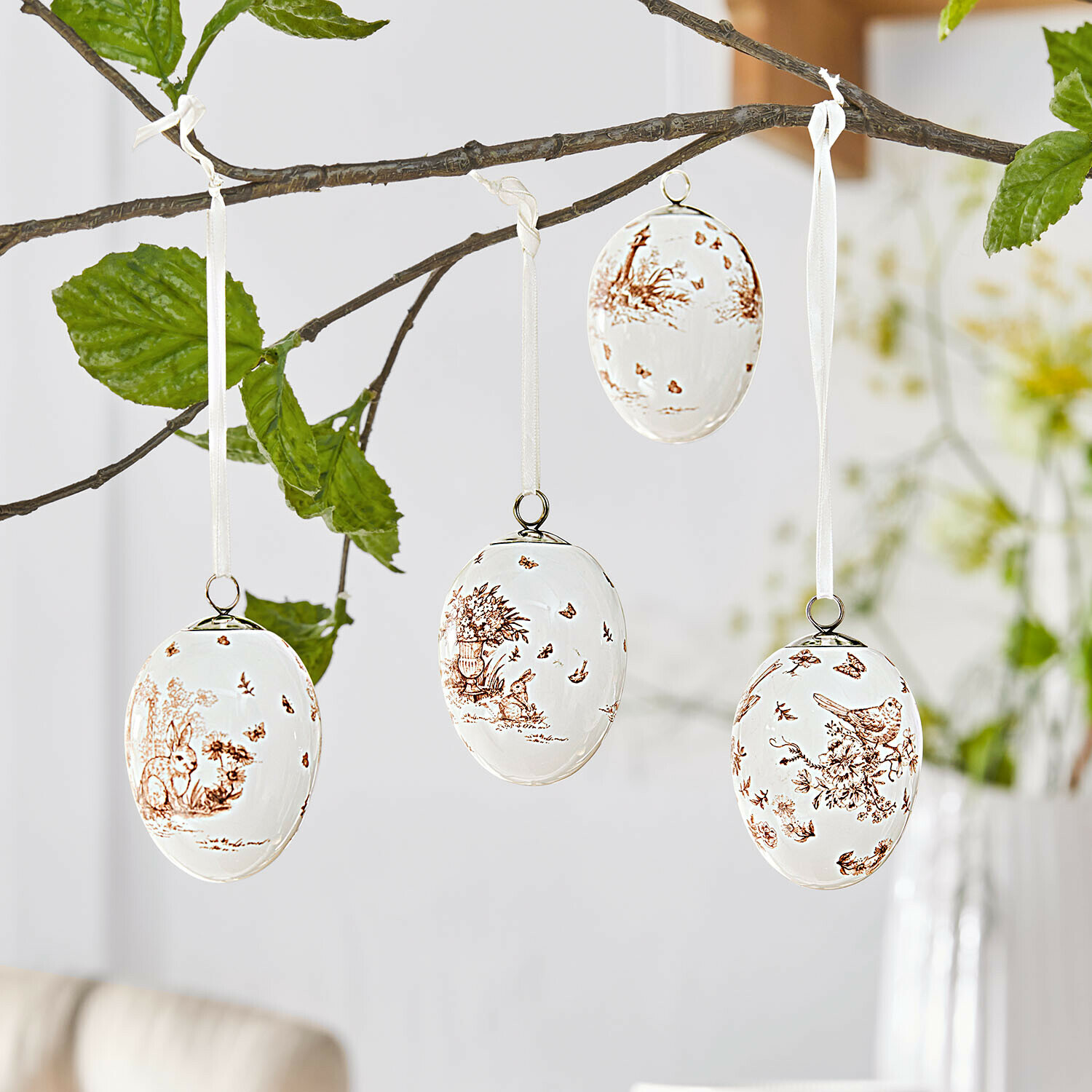 Witte keramische paaseieren met bruine dieren- en plantenmotieven, hangend aan een tak