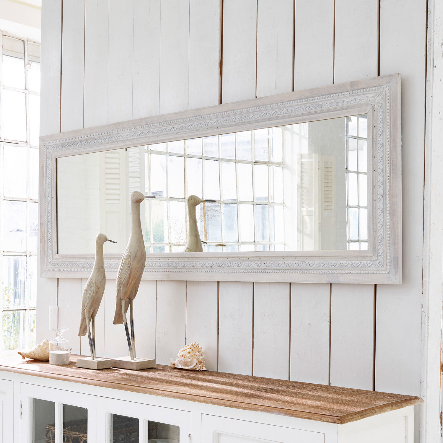 Spiegel Milanu Grote rechthoekige spiegel met witte houten lijst boven een witte kast met houten en schelpen decoraties