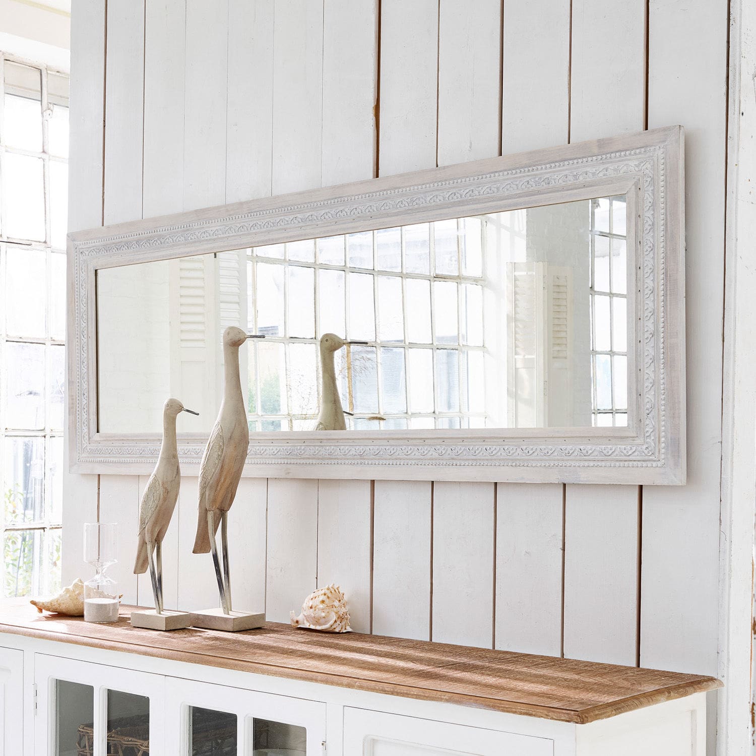 Spiegel Milanu Grote rechthoekige spiegel met witte houten lijst boven een witte kast met houten en schelpen decoraties