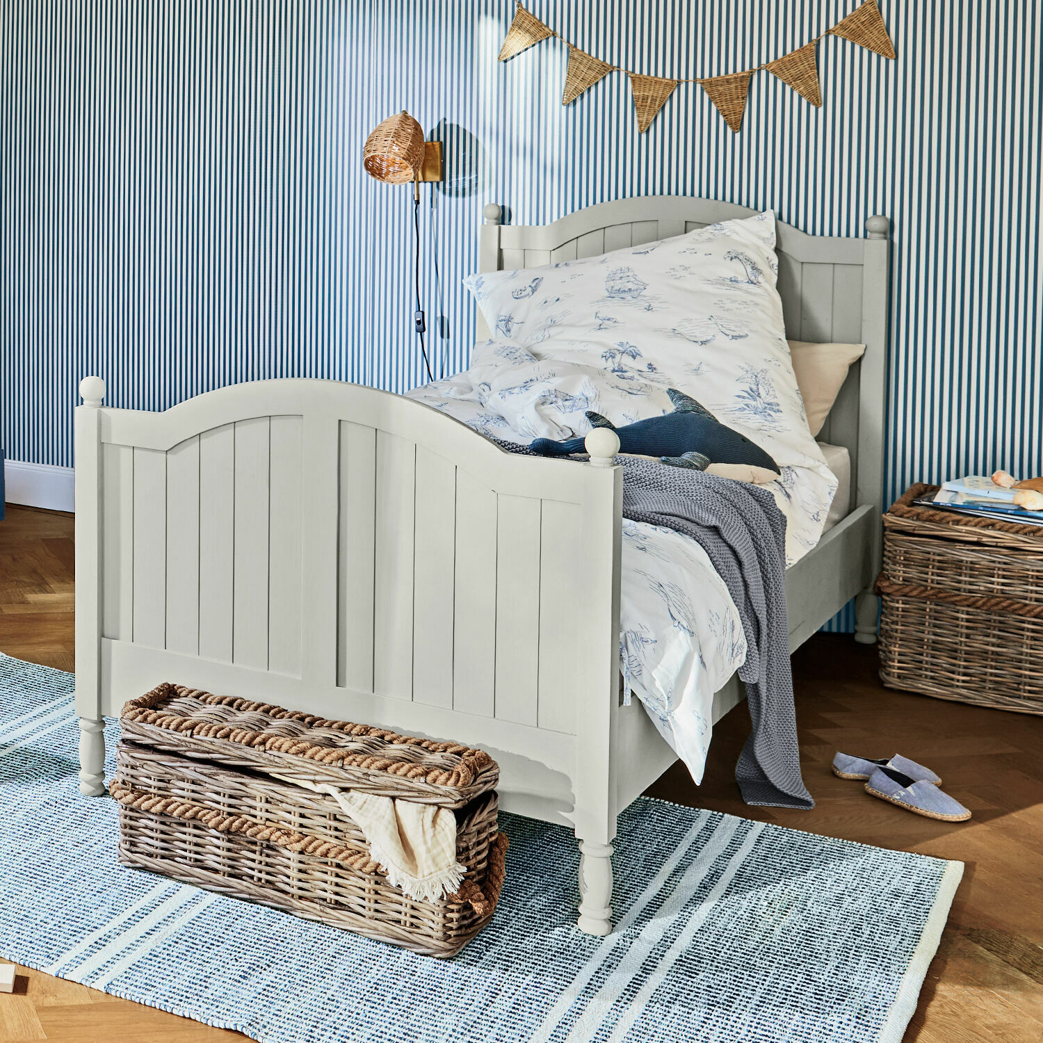 Bed Alarion Grijs houten kinderbed met maritiem beddengoed en rieten mand op blauwe vloerkleed