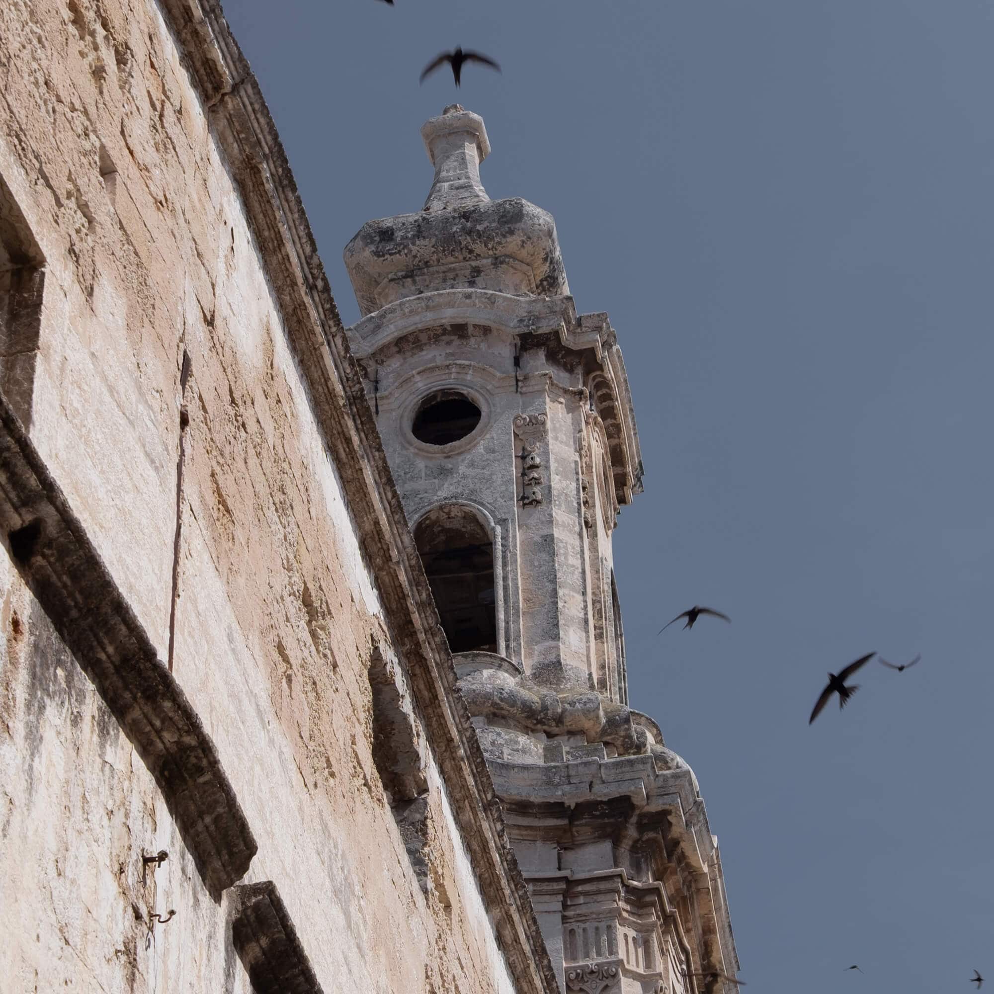 Uitzicht op een oude stenen toren met vogels tegen een blauwe lucht