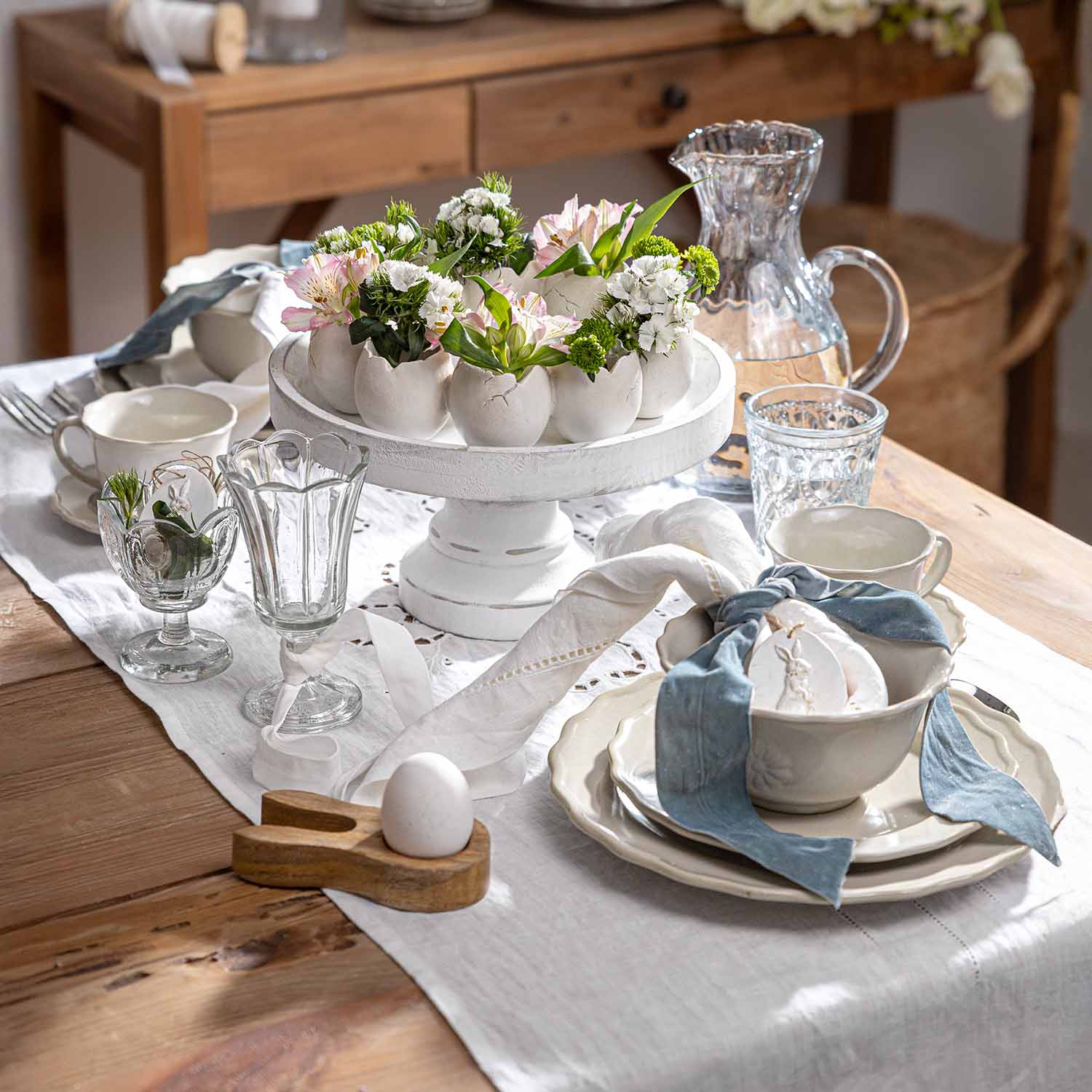 Witte keramische standaard met eivormige bloempotten en bloemen op rustieke houten tafel