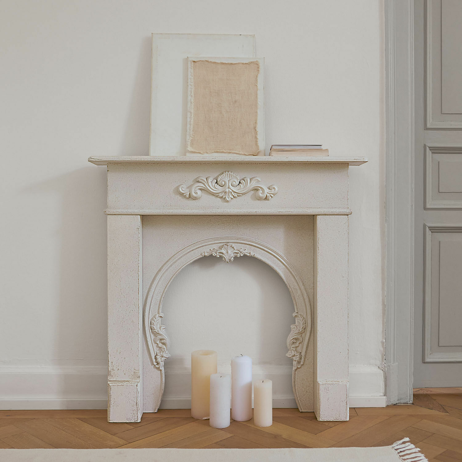 Witte decoratieve schoorsteenmantel met ornamenten en kaarsen op houten vloer in vintage stijl