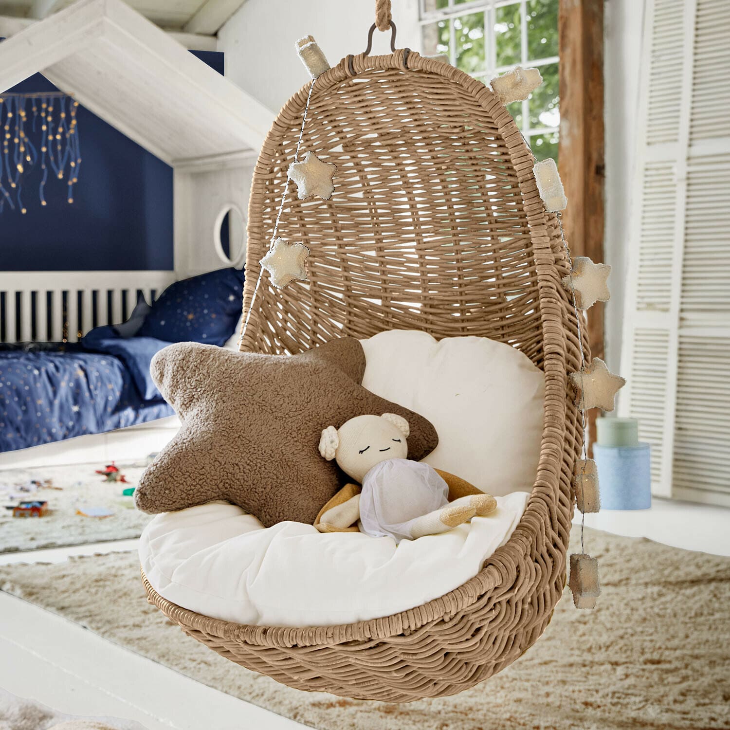 Kinderhangstoel Twinkla Hangstoel van riet met wit kussen en stervormige lichtjes in kinderkamer