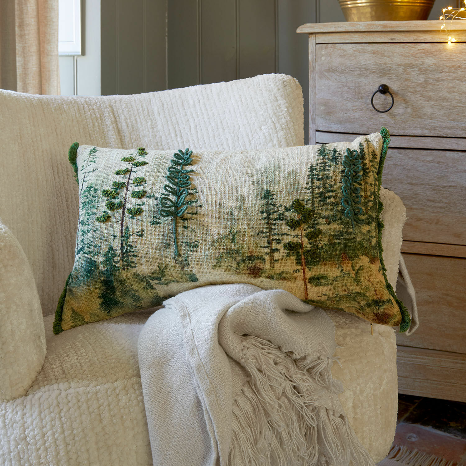 Kussenhoes Kilvora Decoratief kussen met groene bomenprint op beige stof op witte stoel met franjes deken