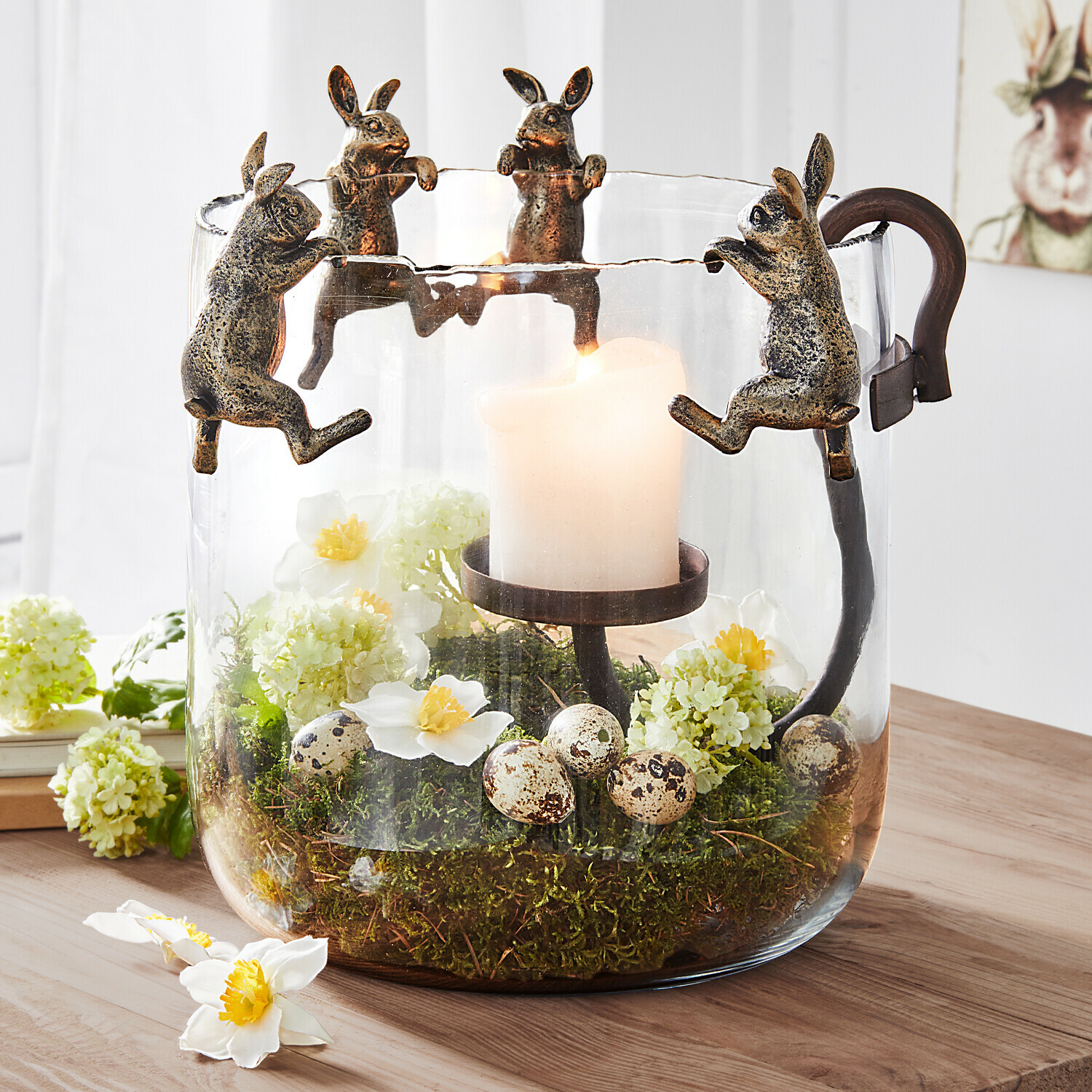 Glazen windlicht met metalen konijntjes, witte kaars en decoratie van mos en eieren, lentestijl