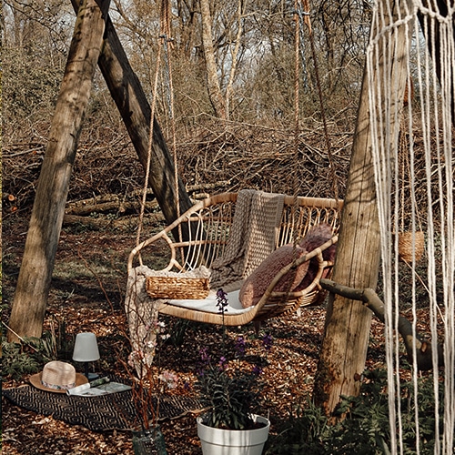 Tuin schommel van natuurlijk riet met kussens en deken tegen een herfstig bosdecor