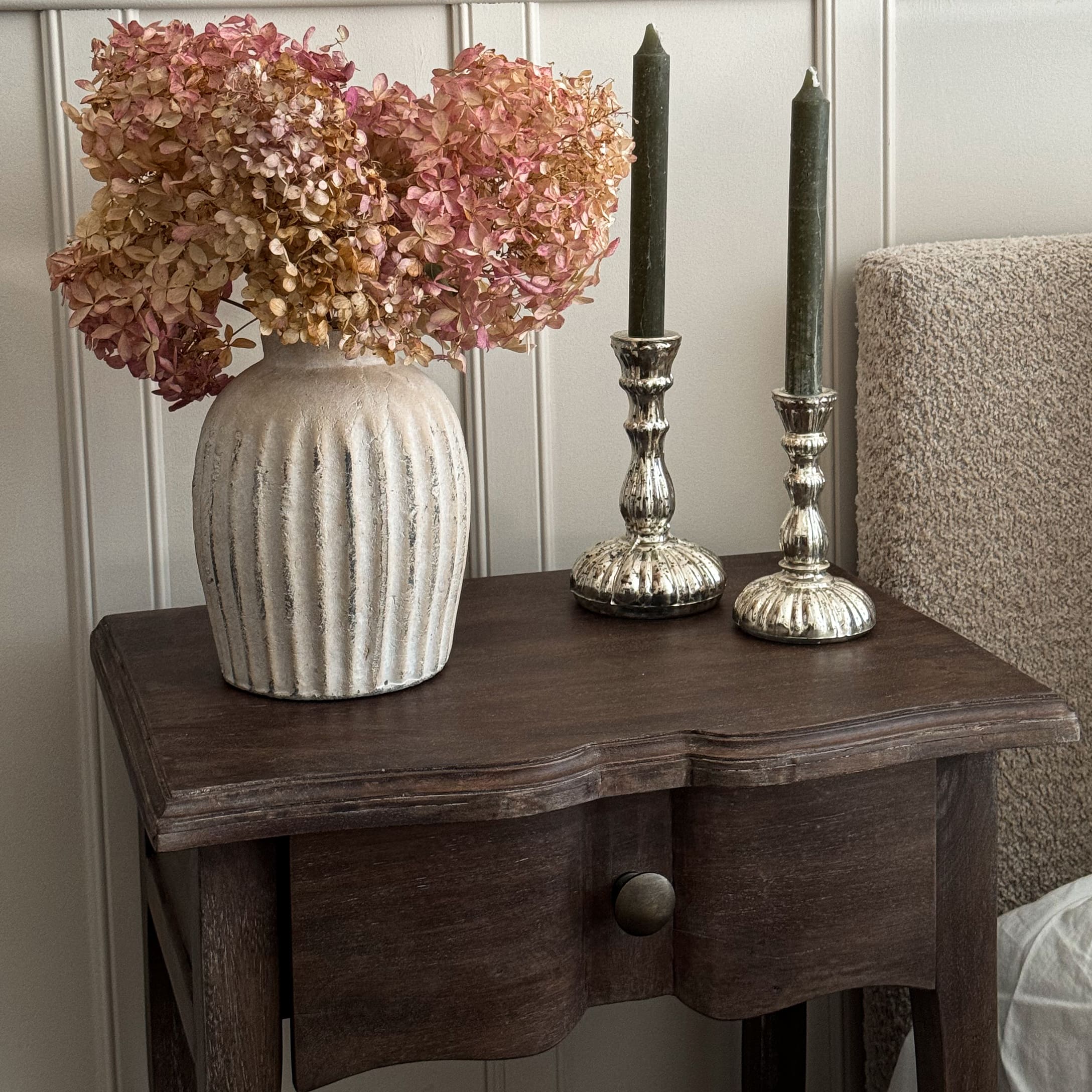 Beige keramische vaas met gedroogde roze bloemen op een donkerhouten tafel als decoratie