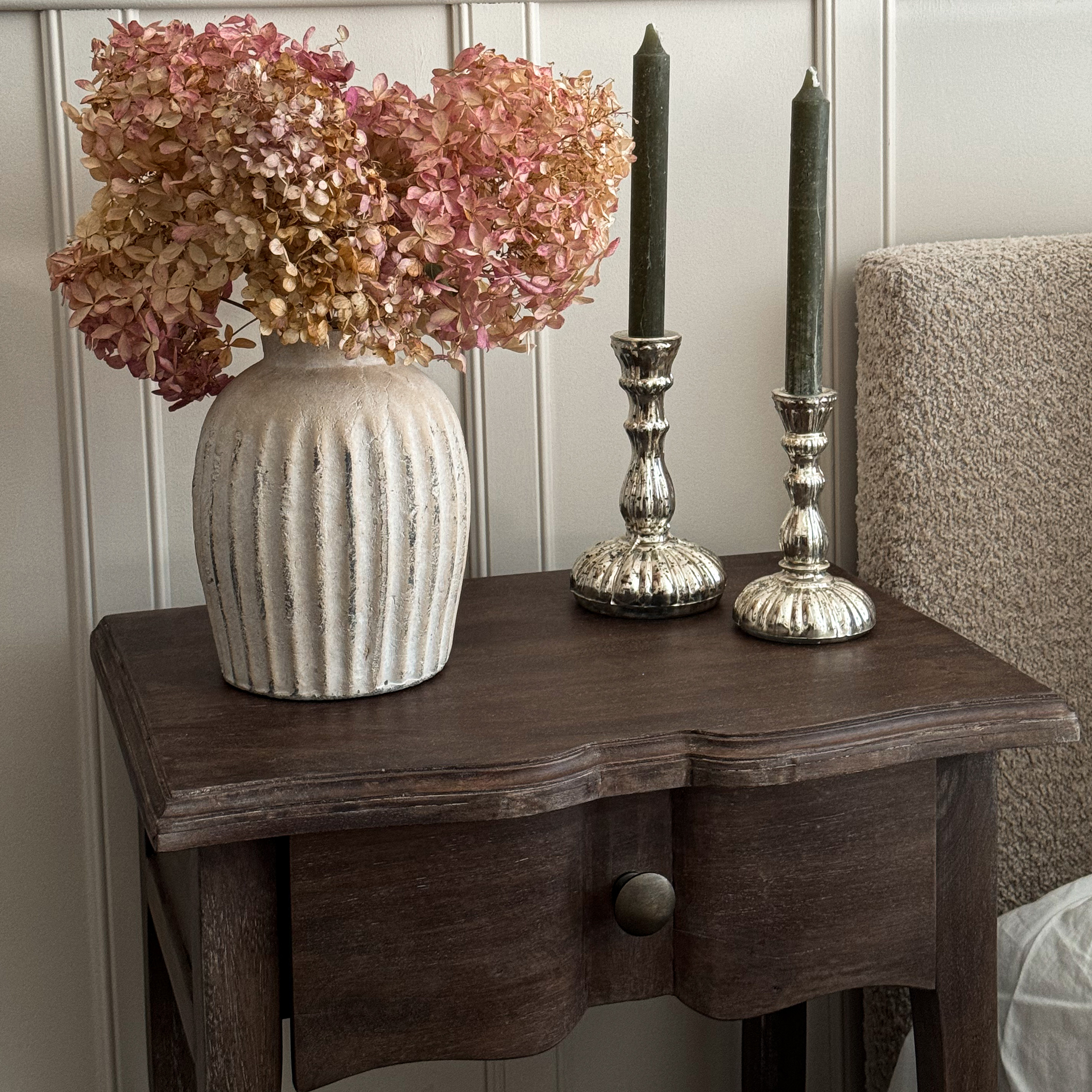 Beige keramische vaas met gedroogde roze bloemen op een donkerhouten tafel als decoratie